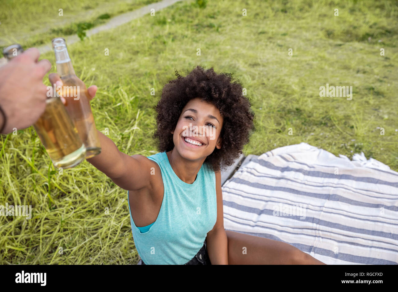 Happy woman sitting outdoors clinking beer bottle Stock Photo