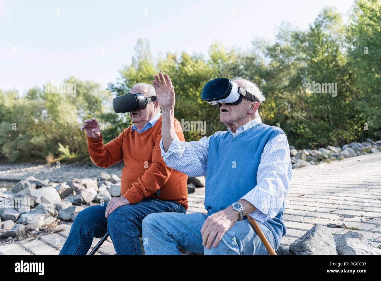 Two old friends sitting by the riverside, using VR glasses Stock Photo