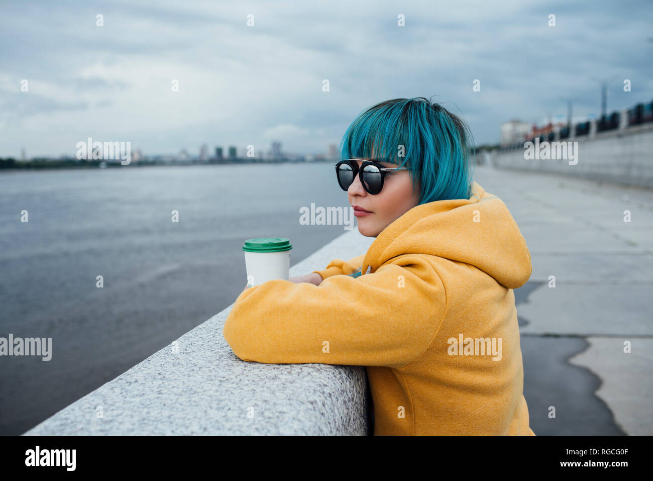 Young woman with dyed blue hair leaning on a wall looking at distance Stock Photo