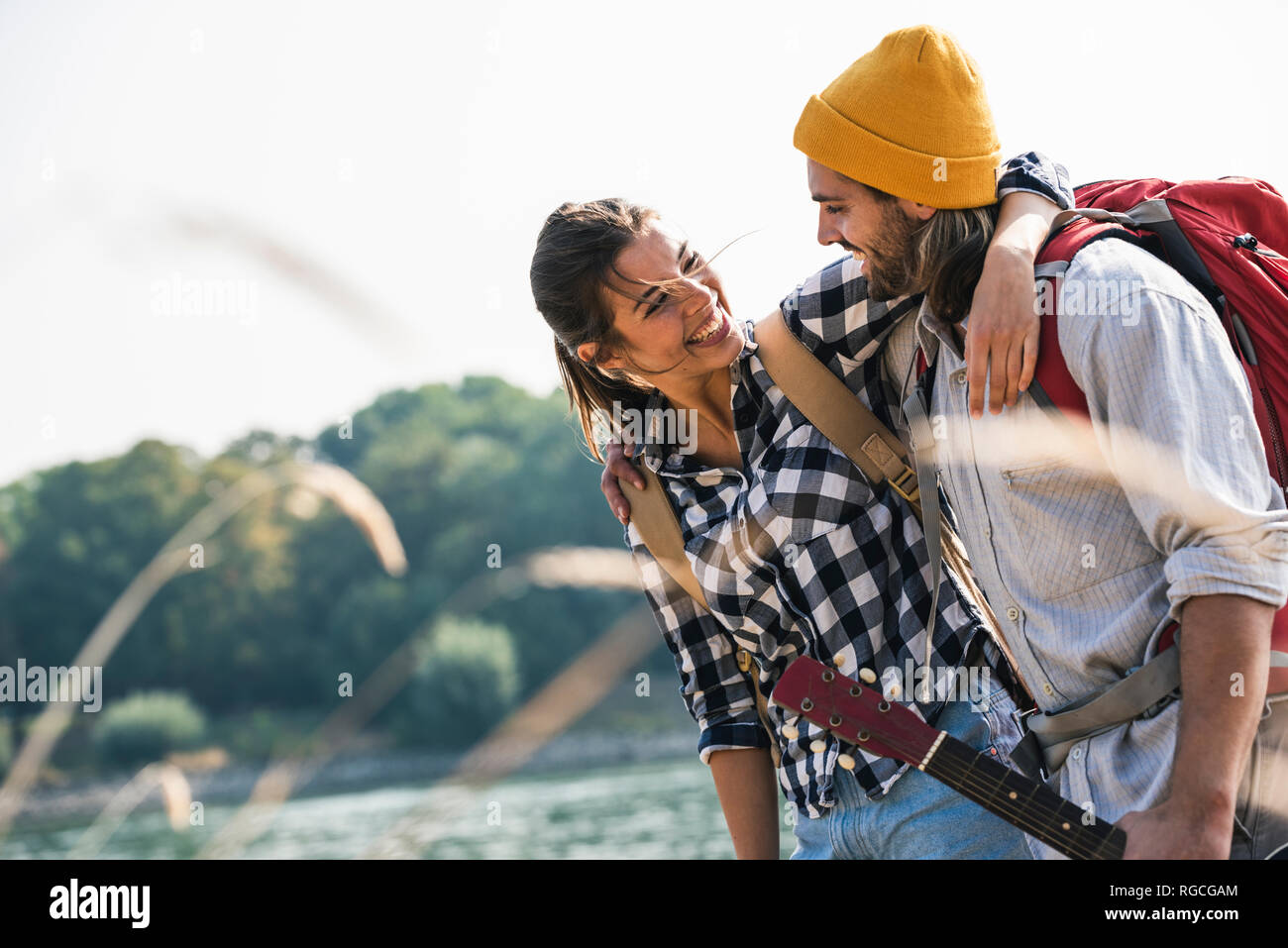 Happy young couple with backpacks and guitar embracing at the riverside Stock Photo