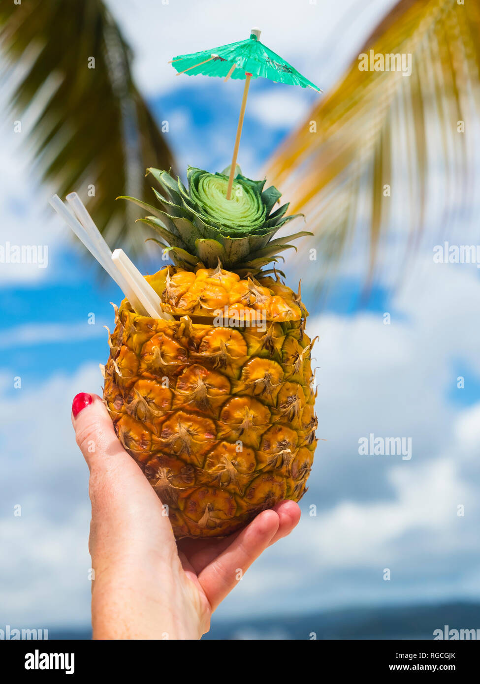 Woman's hand holding fresh pineapple with a straw Stock Photo