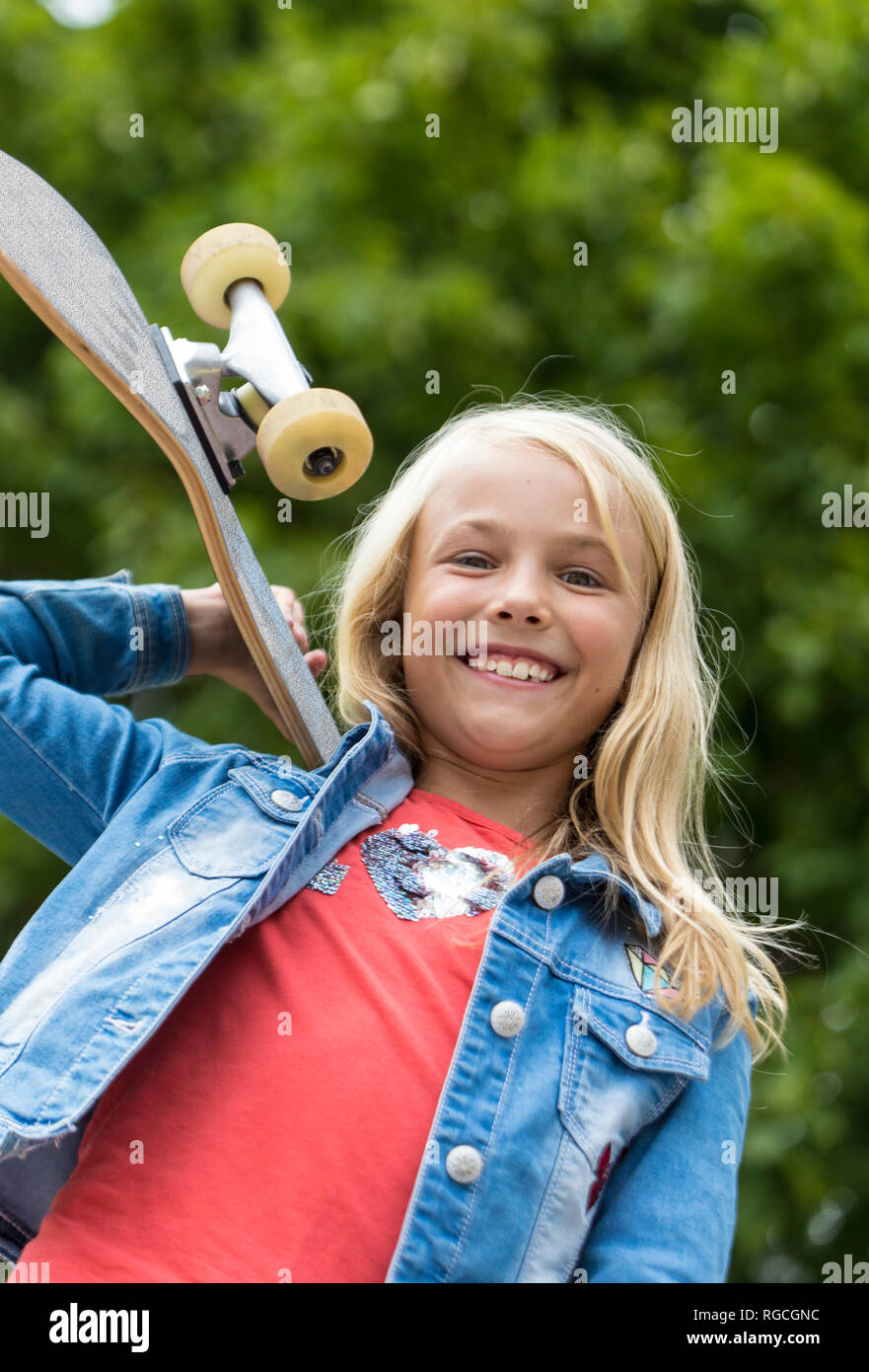 Portrait of proud blond girl with skateboard on her shoulder Stock Photo