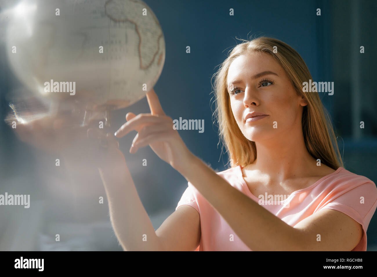 Portrait of young woman looking and pointing at globe Stock Photo