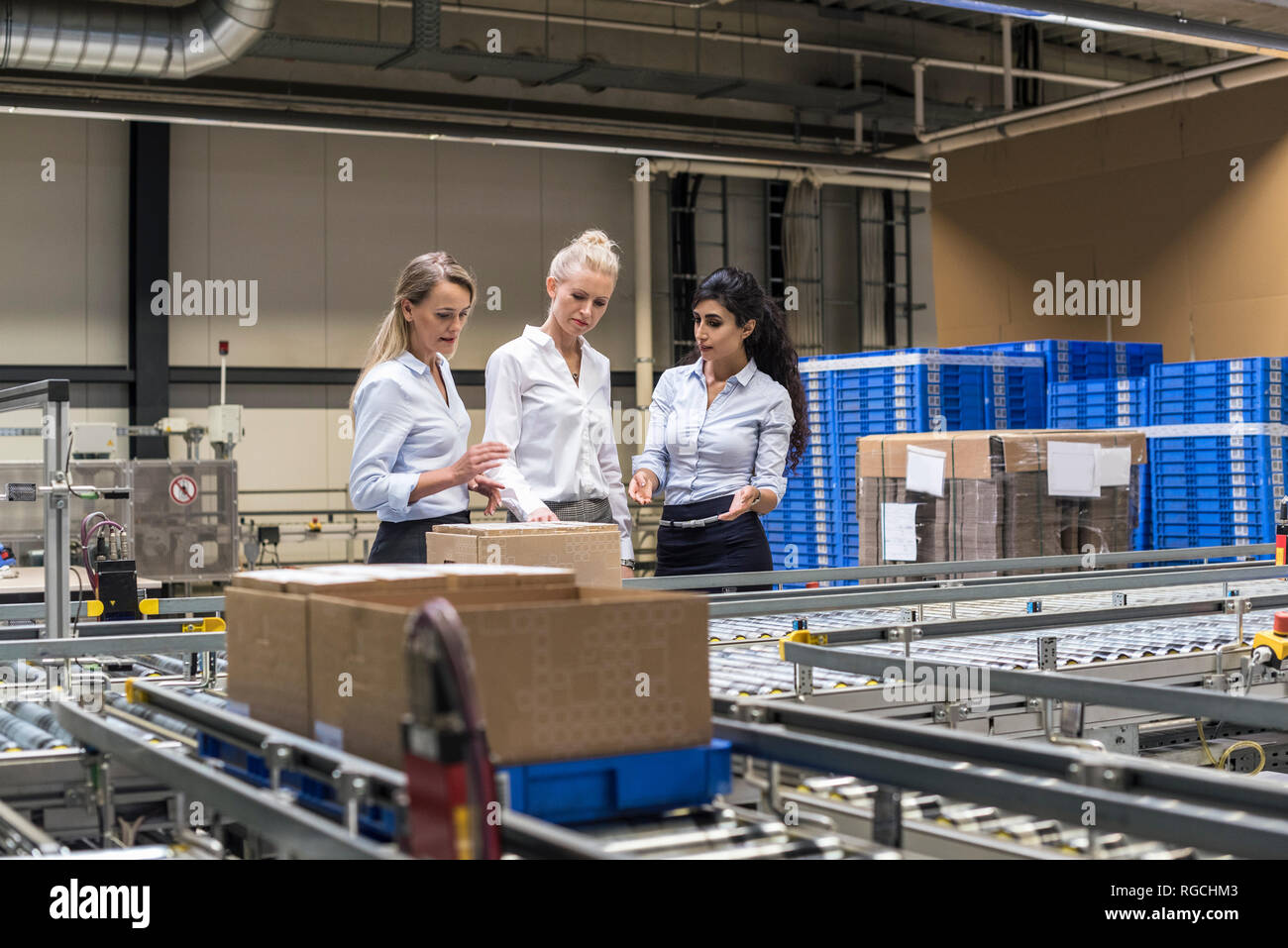 Three women discussing at conveyor belt in factory Stock Photo