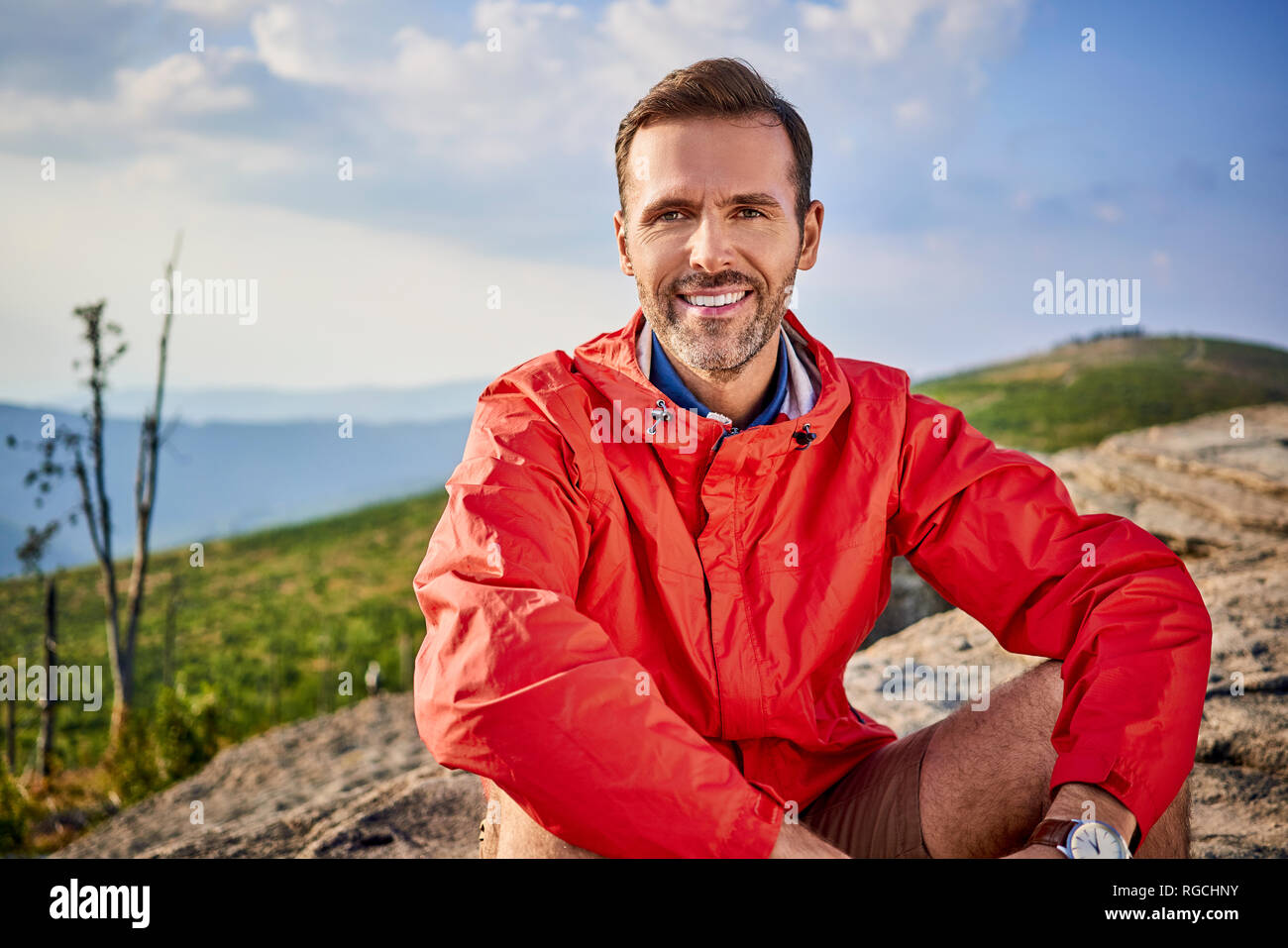Portrait of smiling man sitting on rock during hiking trip Stock Photo