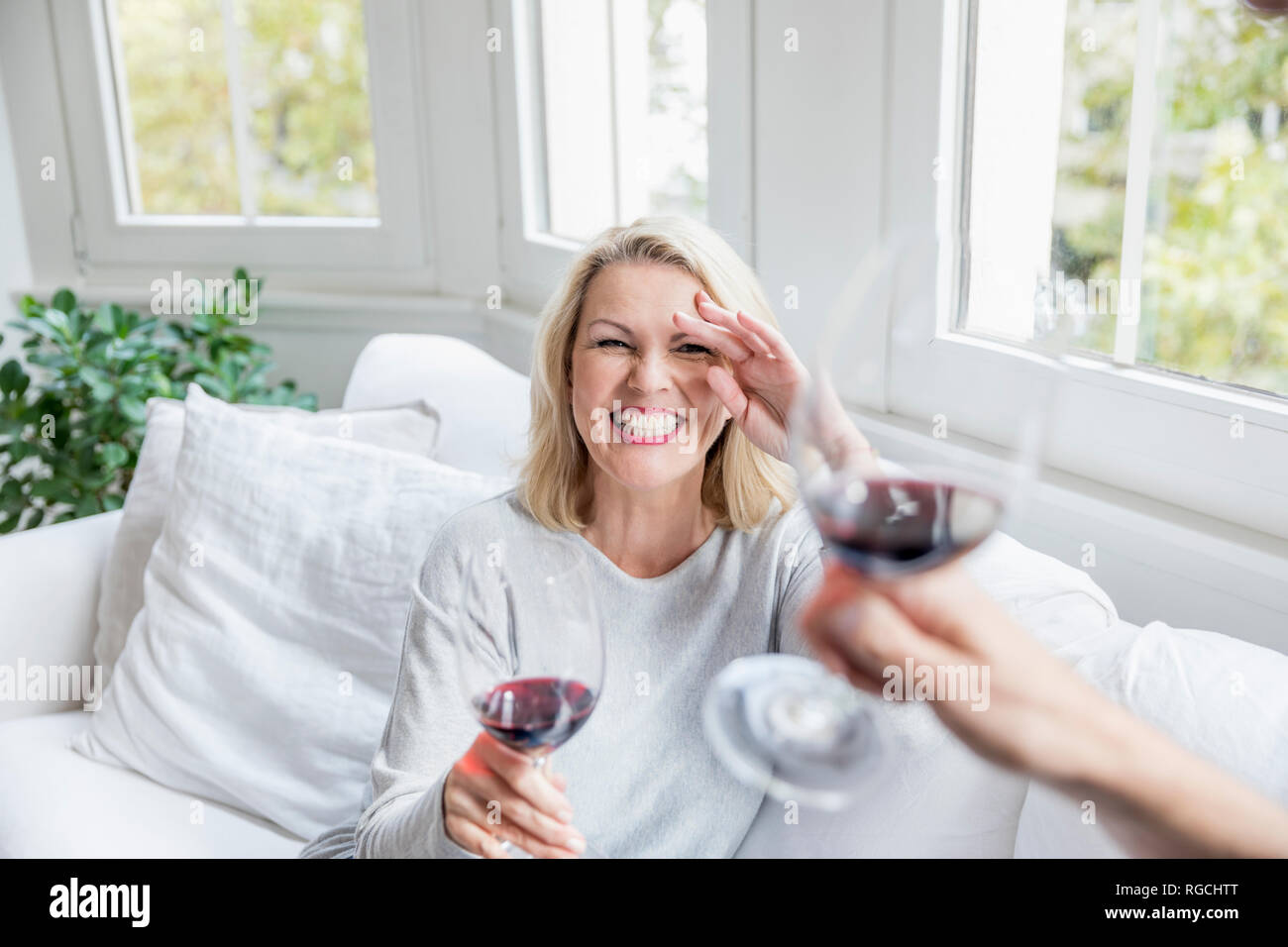 Portrait of laughing blond mature woman toasting with red wine at home Stock Photo