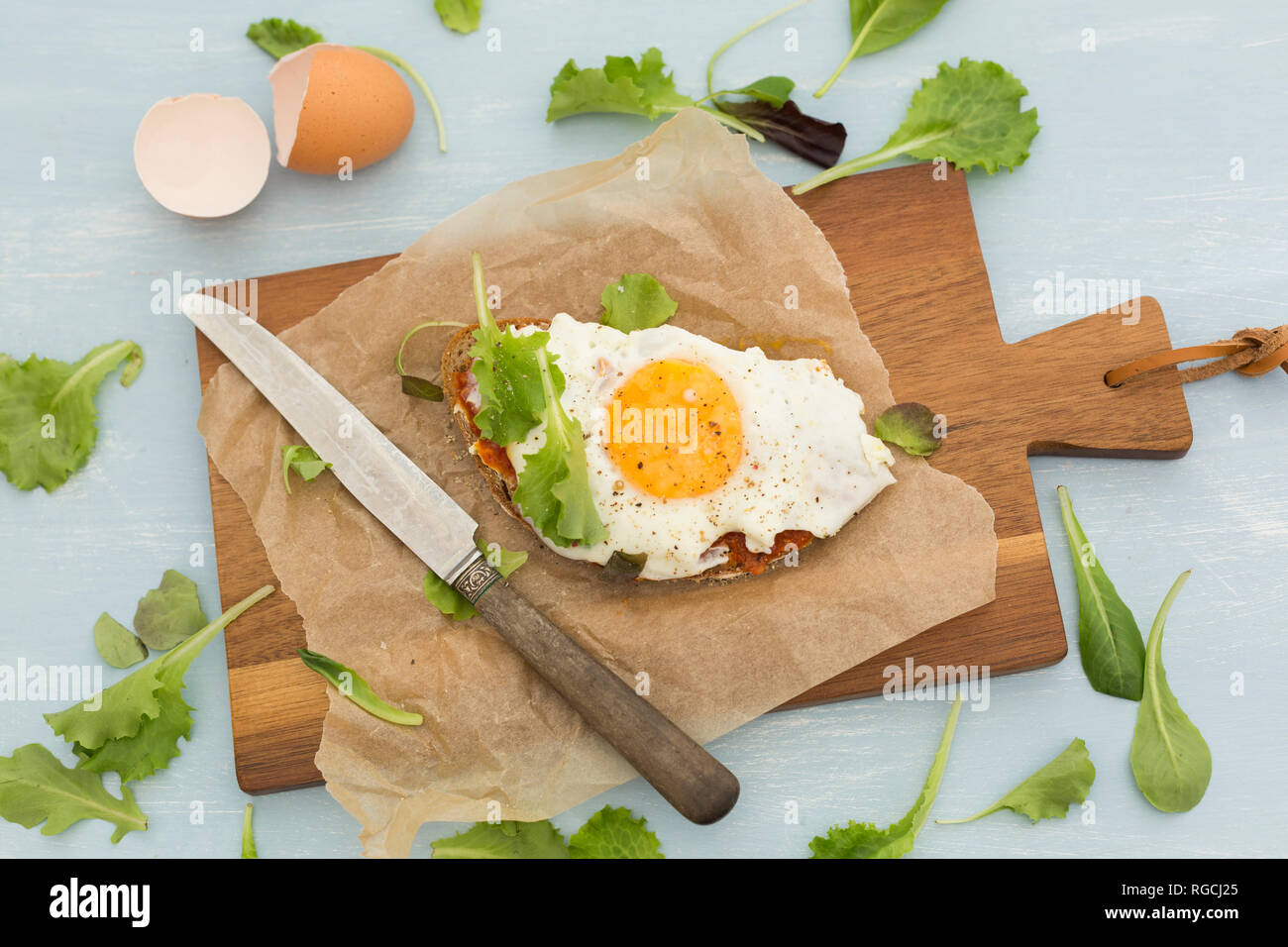 Fried egg on slice of brown bread coated with paprika cream on baking paper Stock Photo