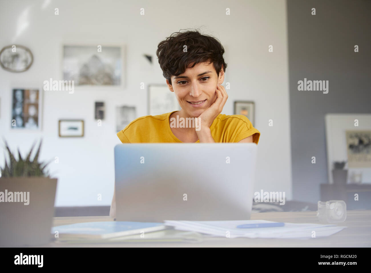 Portrait of smiling woman at home sitting at table using laptop Stock Photo