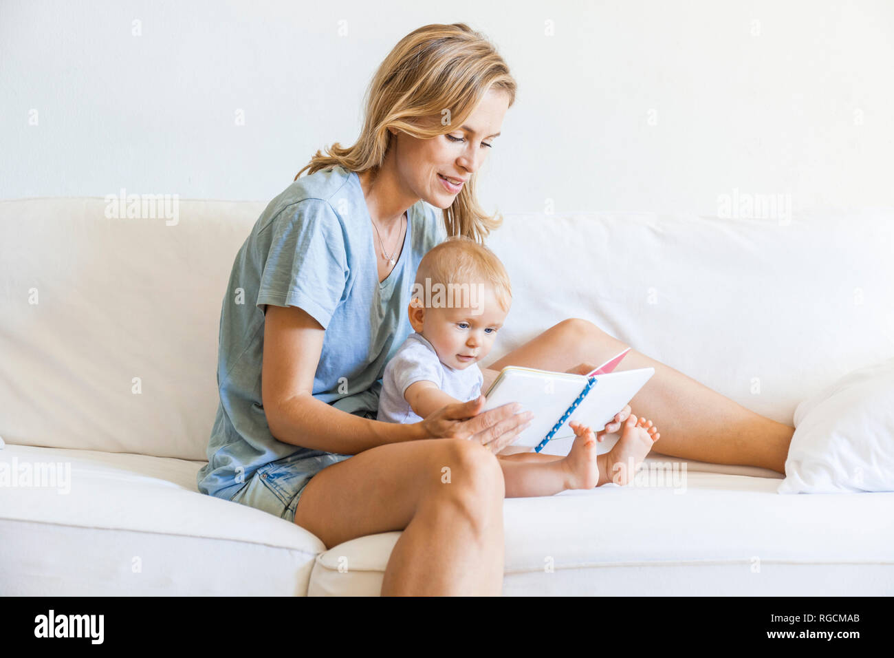 Mother and baby girl sitting on couch looking at picture book Stock Photo
