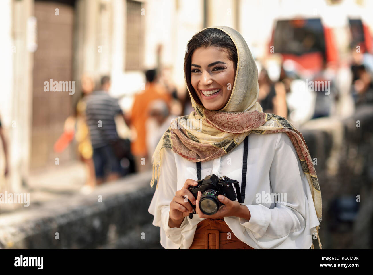 Spain, Granada, young Arab tourist woman wearing hijab, using camera during sightseeing in the city Stock Photo