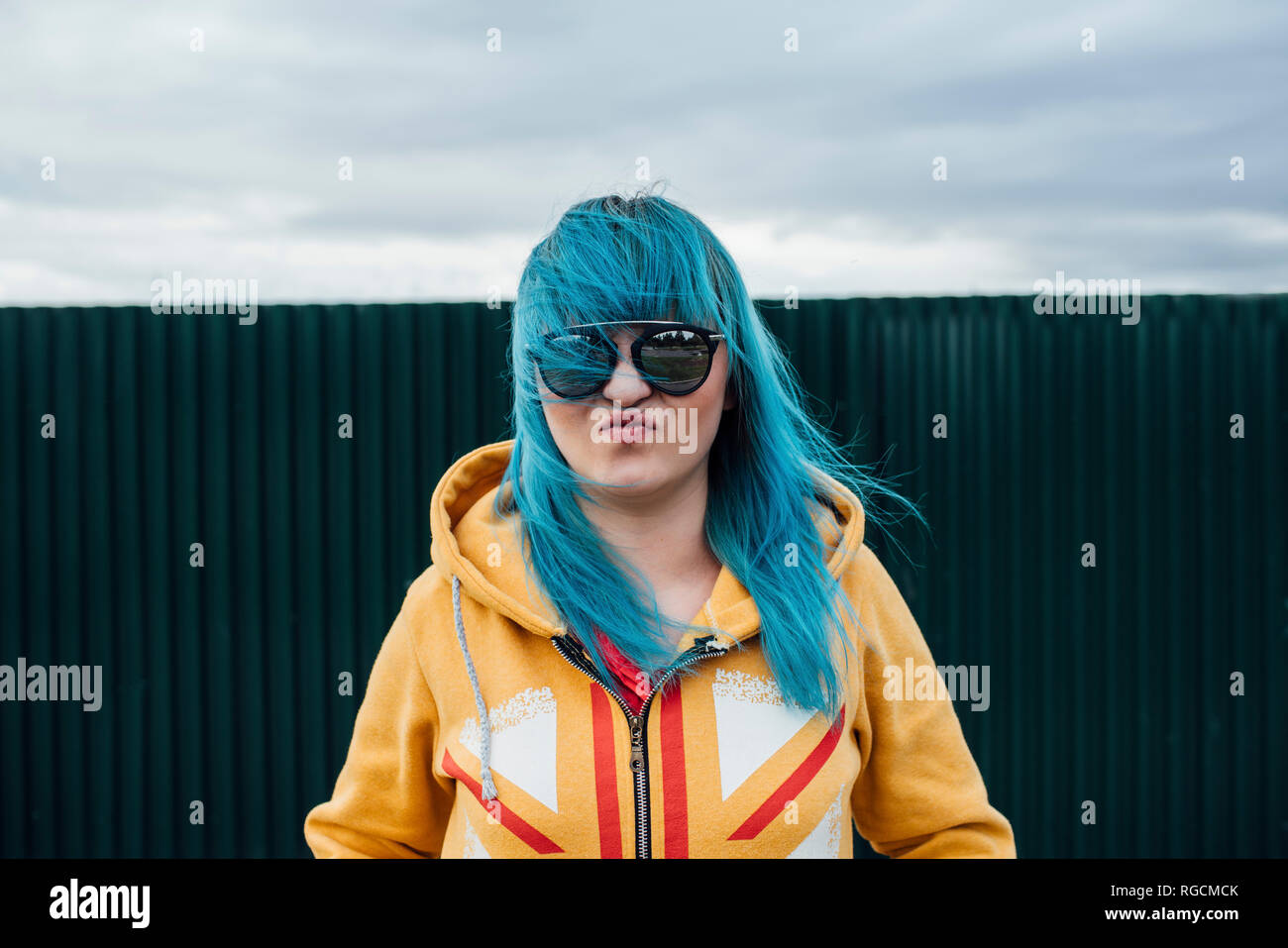 Portrait of young woman with dyed blue hair wearing sunglasses and hooded jacket Stock Photo