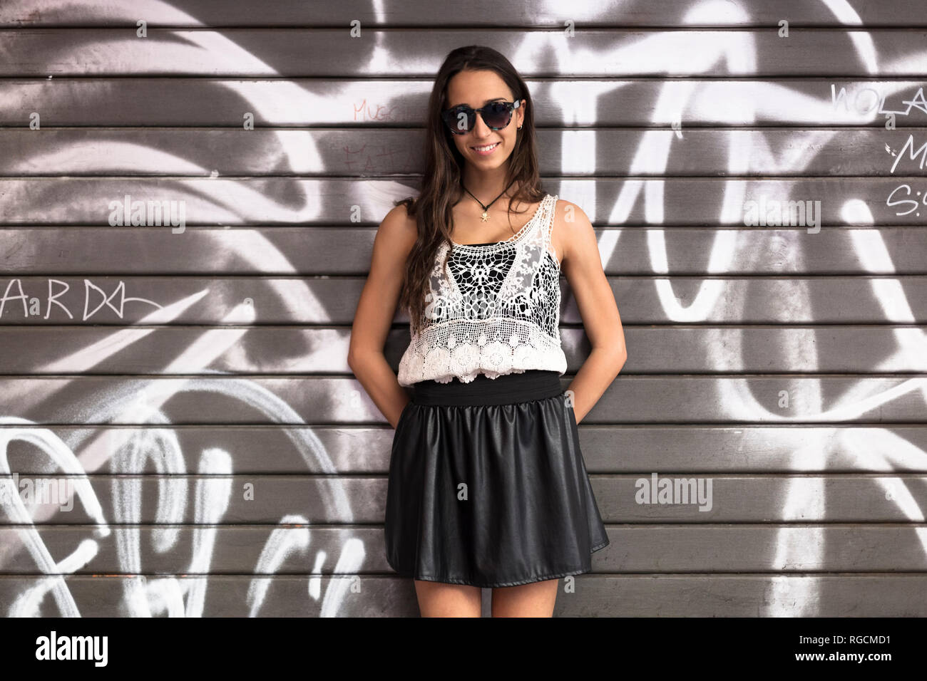 Portrait of fashionable young woman wearing sunglasses standing in front of graffito Stock Photo