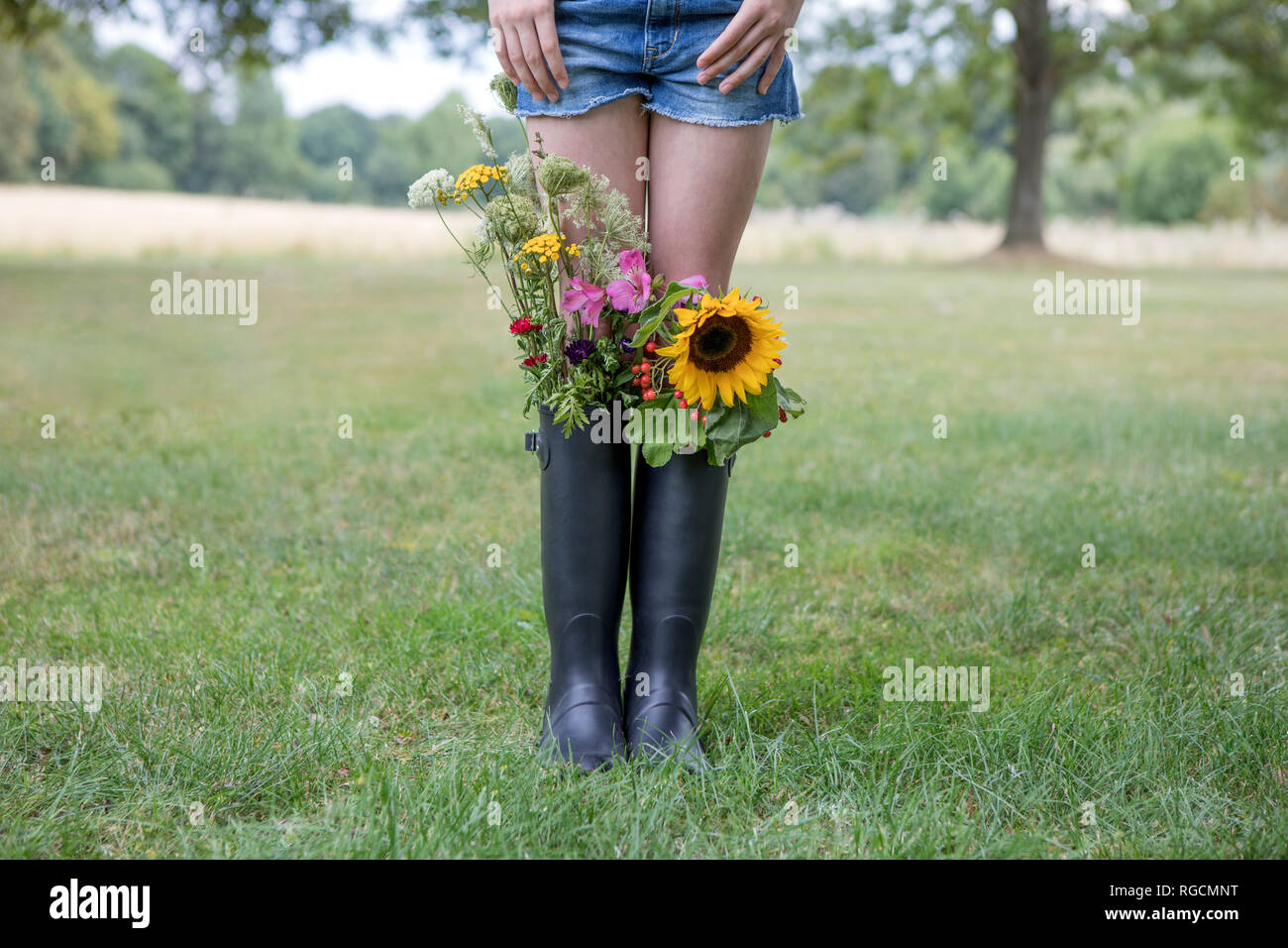 Legs of girl standing on a meadow with bunches of flowers in her rubber ...