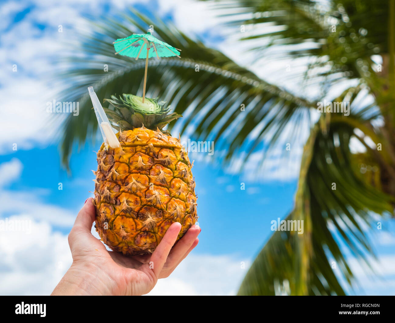 Woman's hand holding fresh pineapple with a straw Stock Photo