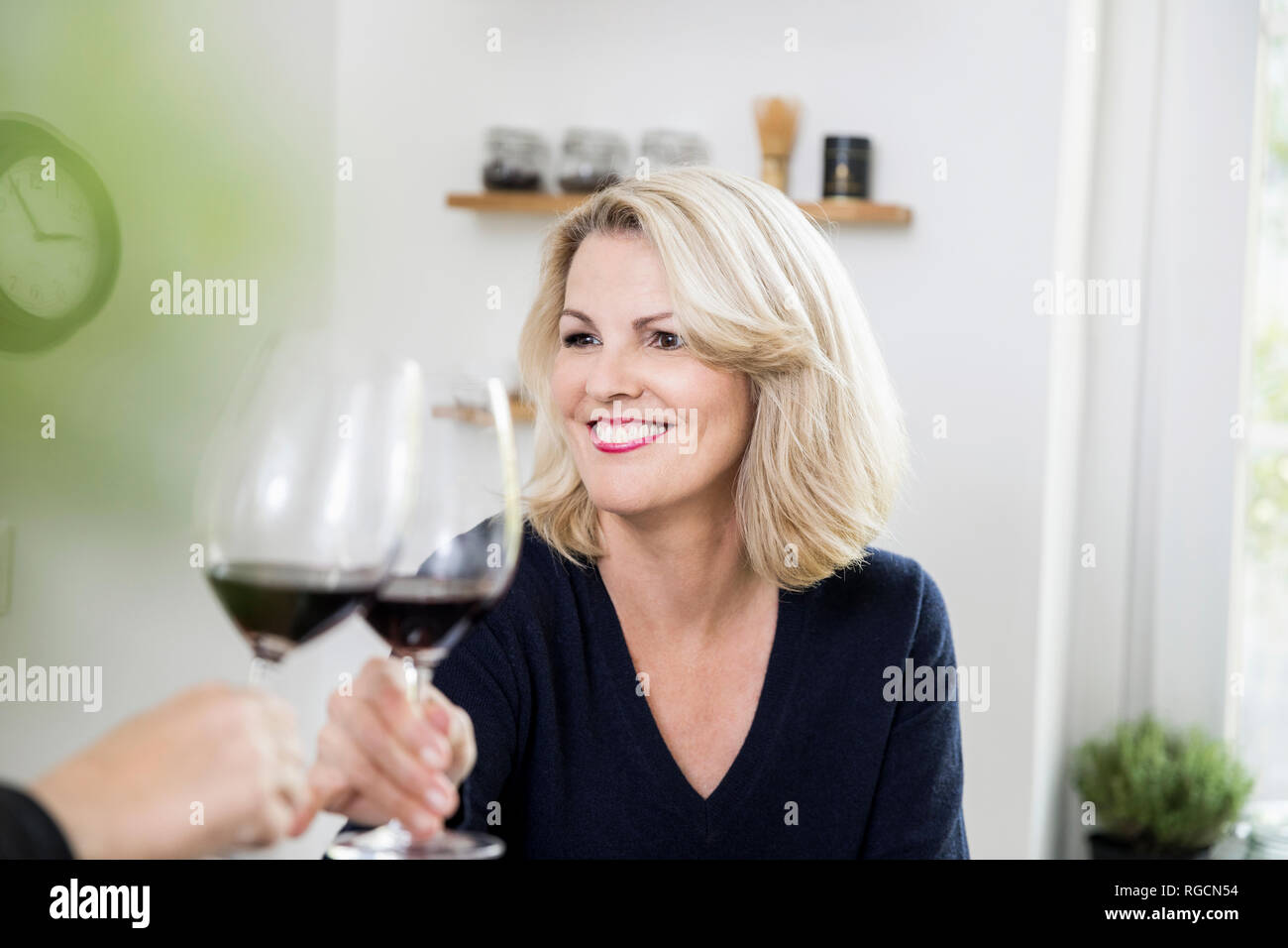 Portrait of smiling blond mature woman toasting with red wine at home Stock Photo