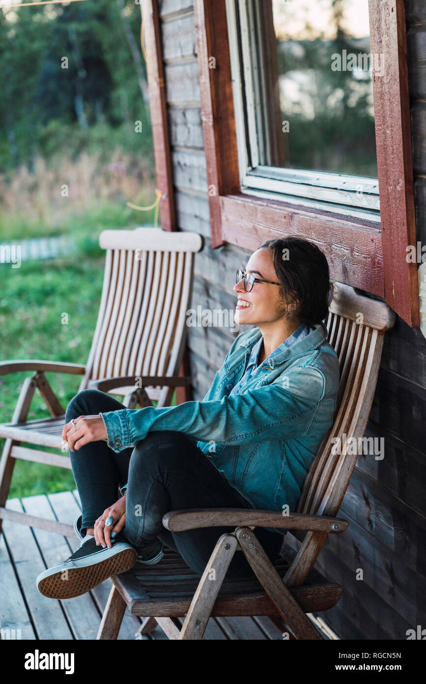 Happy young woman sitting on veranda of a wooden house Stock Photo - Alamy