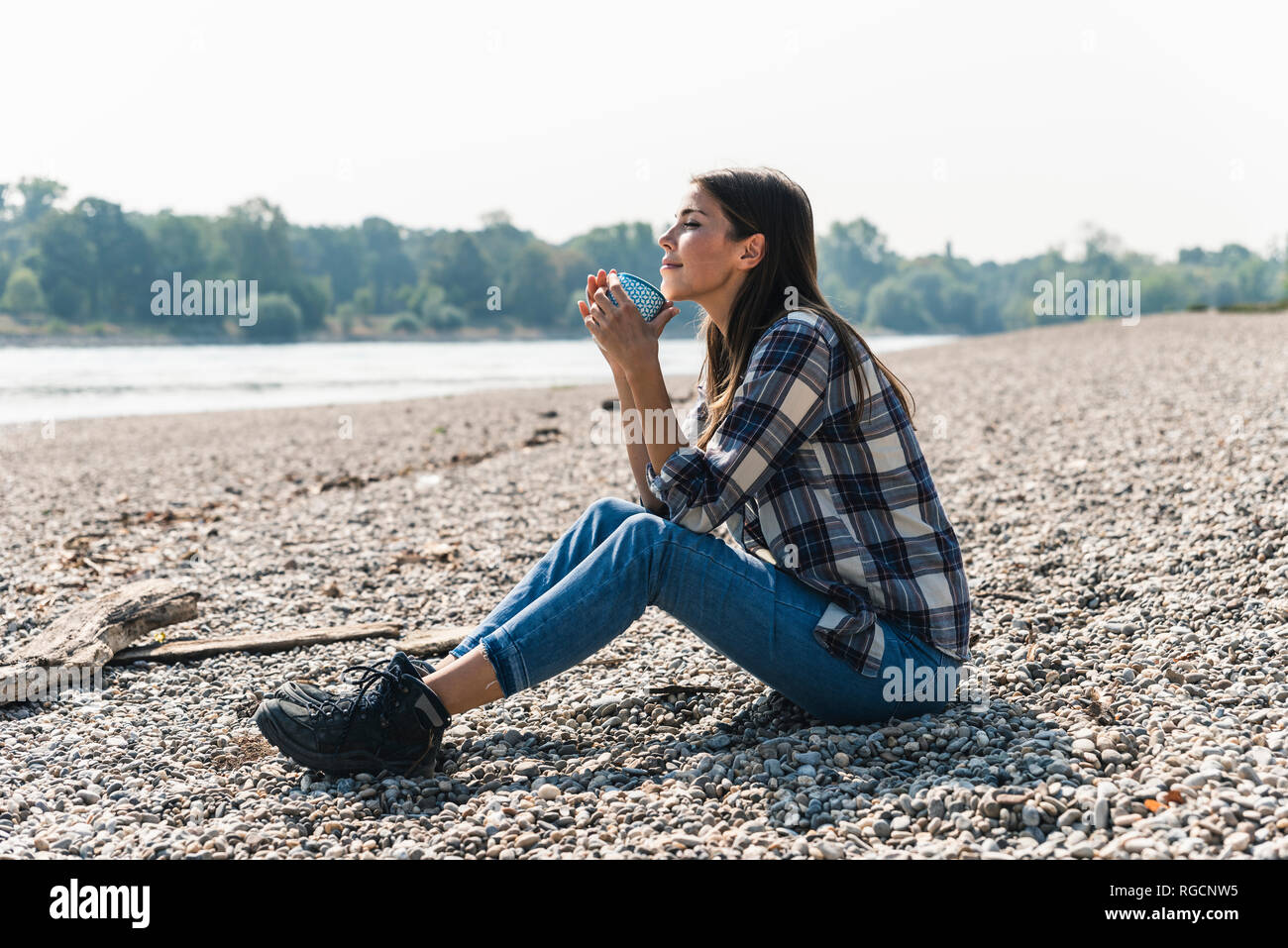 Relaxed young woman holding a mug sitting at the riverside Stock Photo