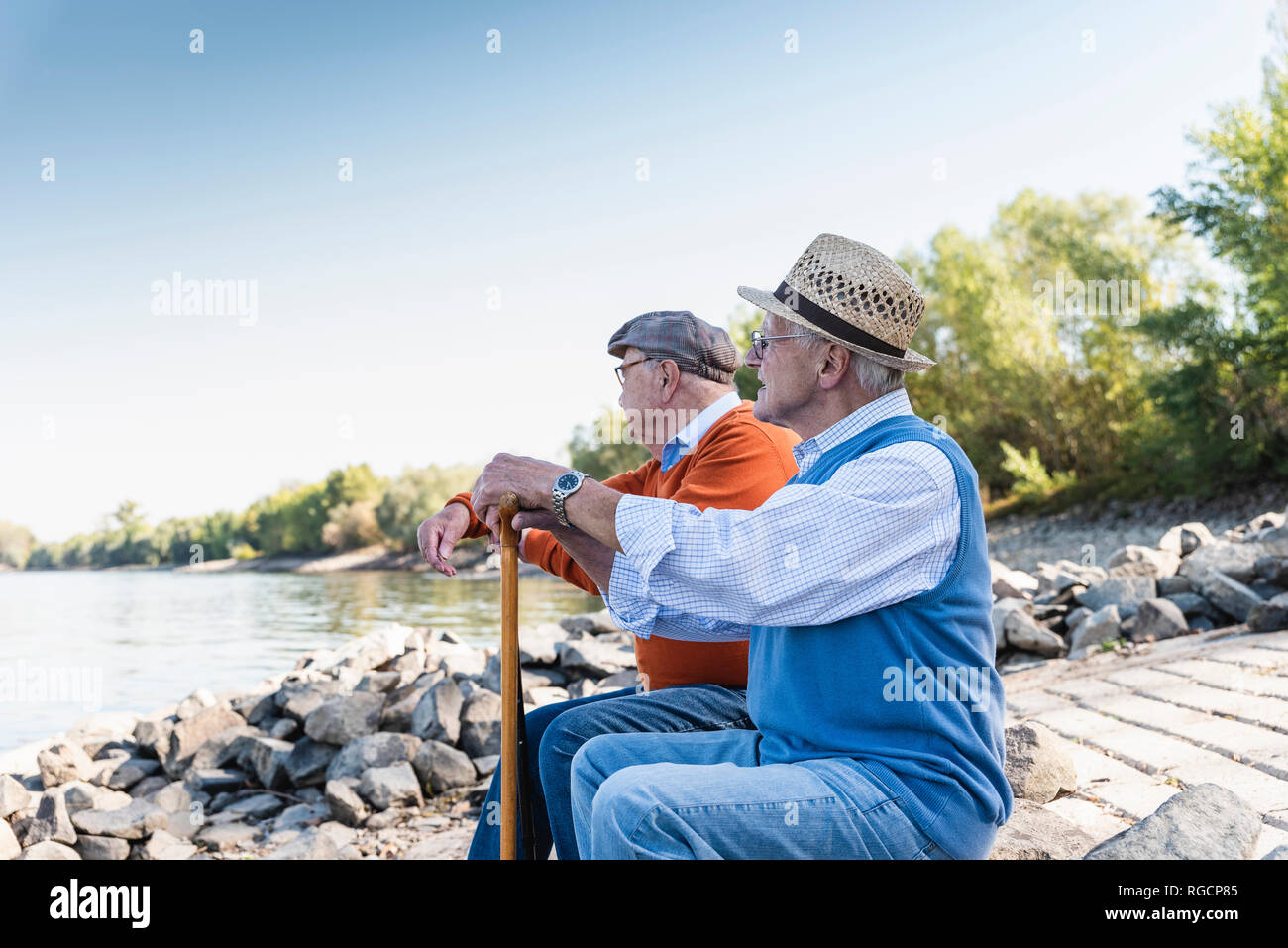 Two old friends sitting on a tree trunk, watching the river Stock Photo