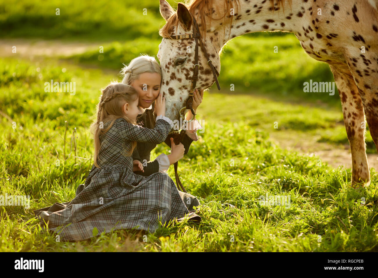 Horse and little girl cuddle with the woman, summer background with green grass Stock Photo