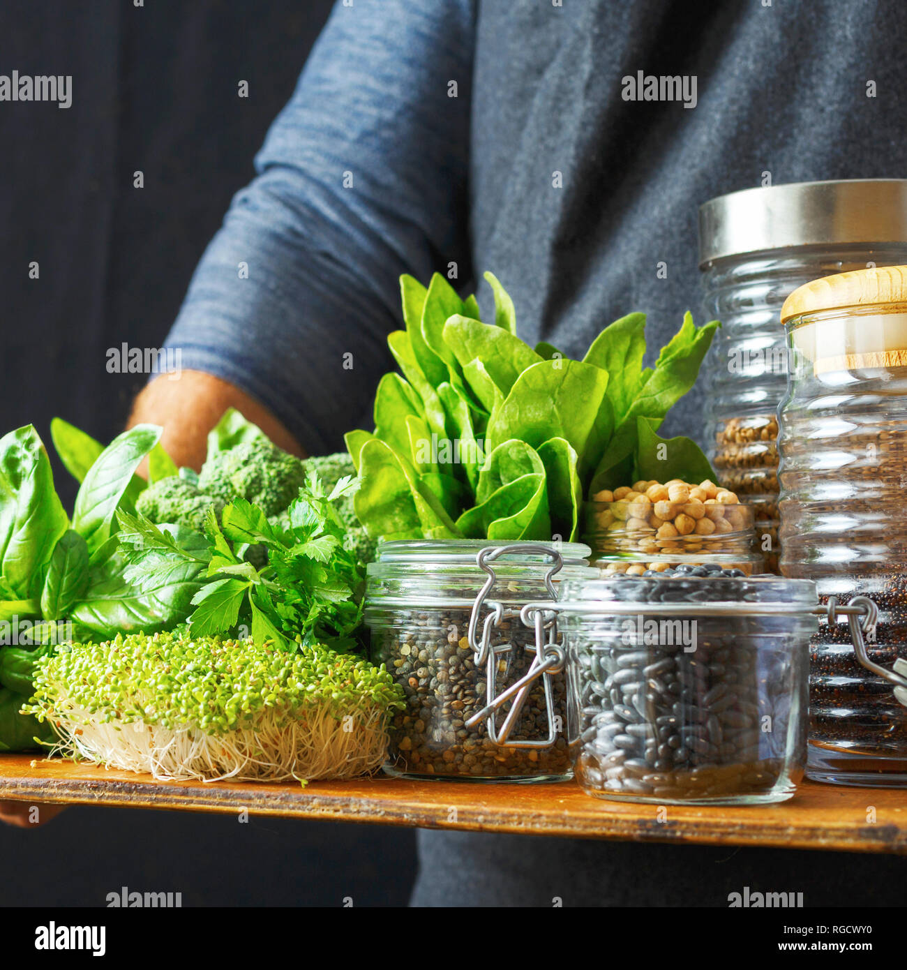 Healthy food, source of protein for vegetarians: vegetable greens, groats, seeds in glass jars in hands man Stock Photo