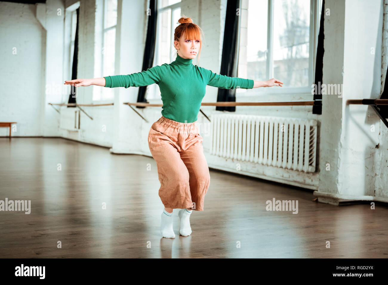 Pretty red haired girl in orange trousers practicing yoga in a gym Stock Photo