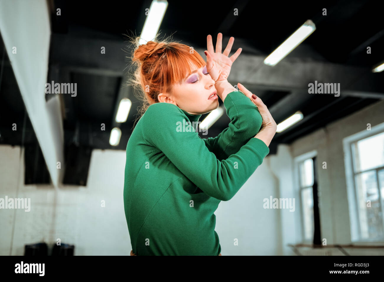 Young red-haired professional choreographer with bright makeup looking flexible Stock Photo