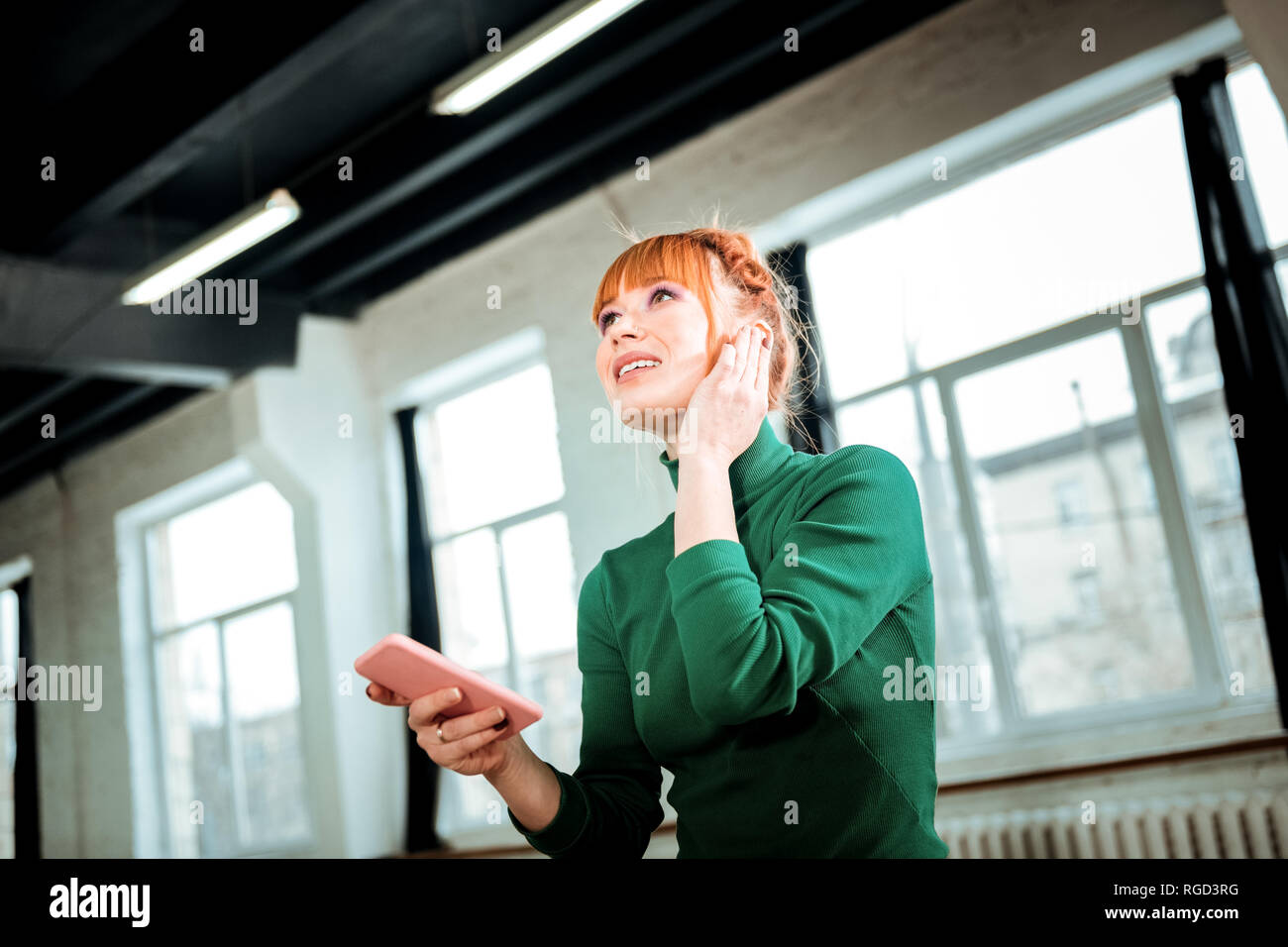 Red-haired professional yoga instructor in a green turtleneck speaking on the phone Stock Photo