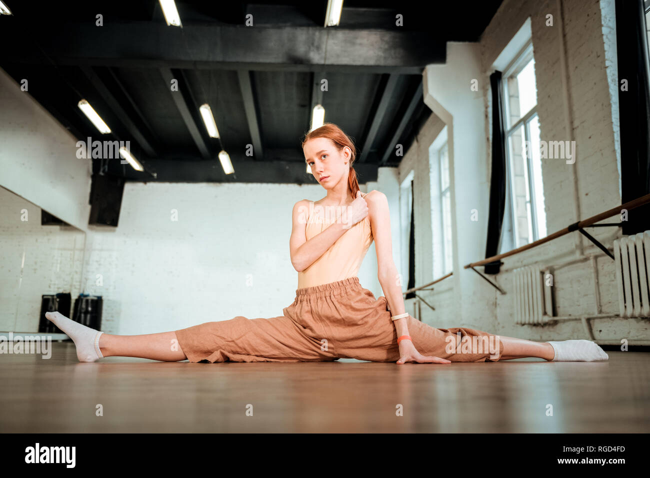 Cute red-haired teenager in orange pants looking thoughtful Stock Photo