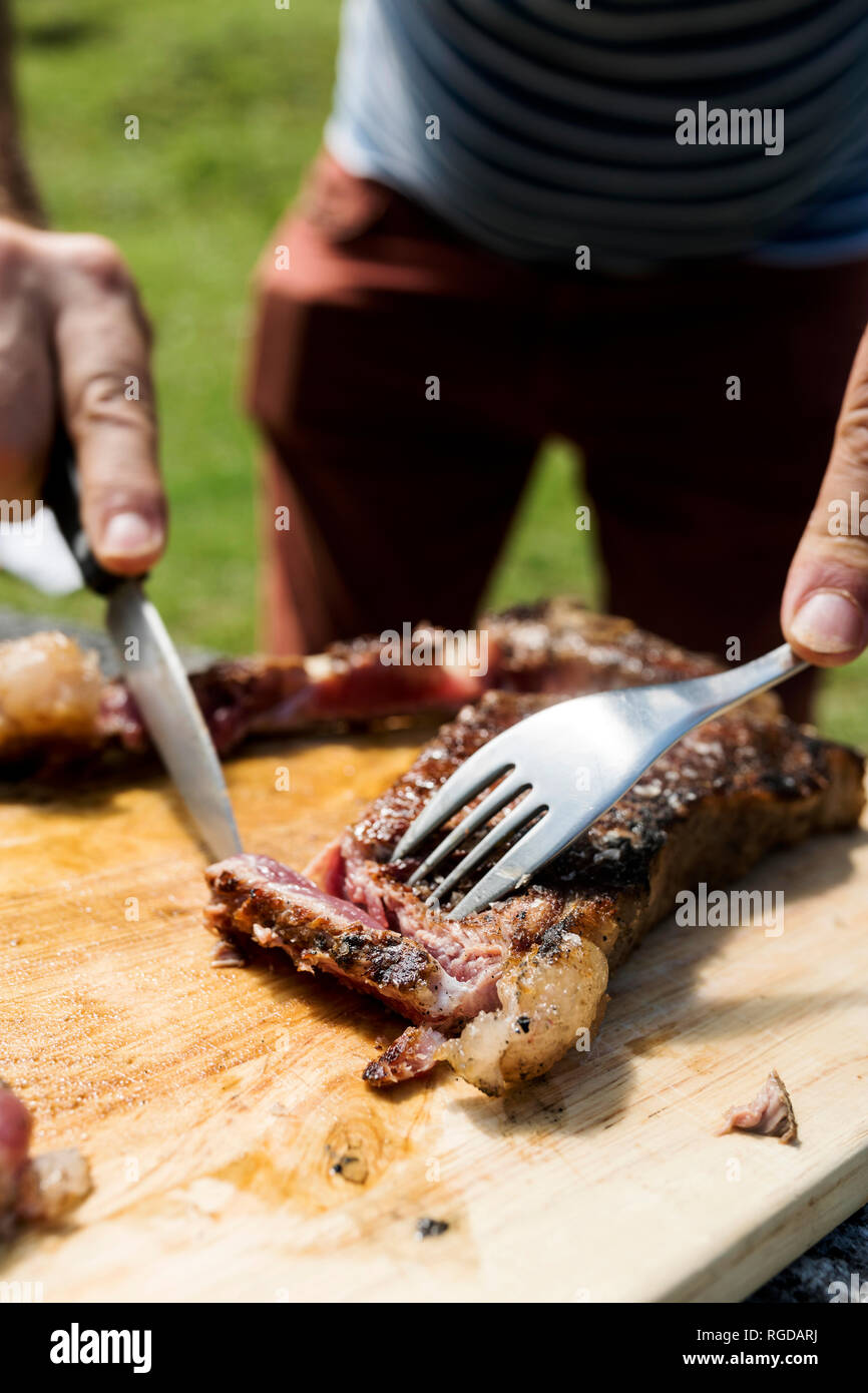 Premium Photo  Man cuts of fresh piece of meat on a wooden cutting board  in the home kitchen. a man in a striped apron with a big knife in his hands