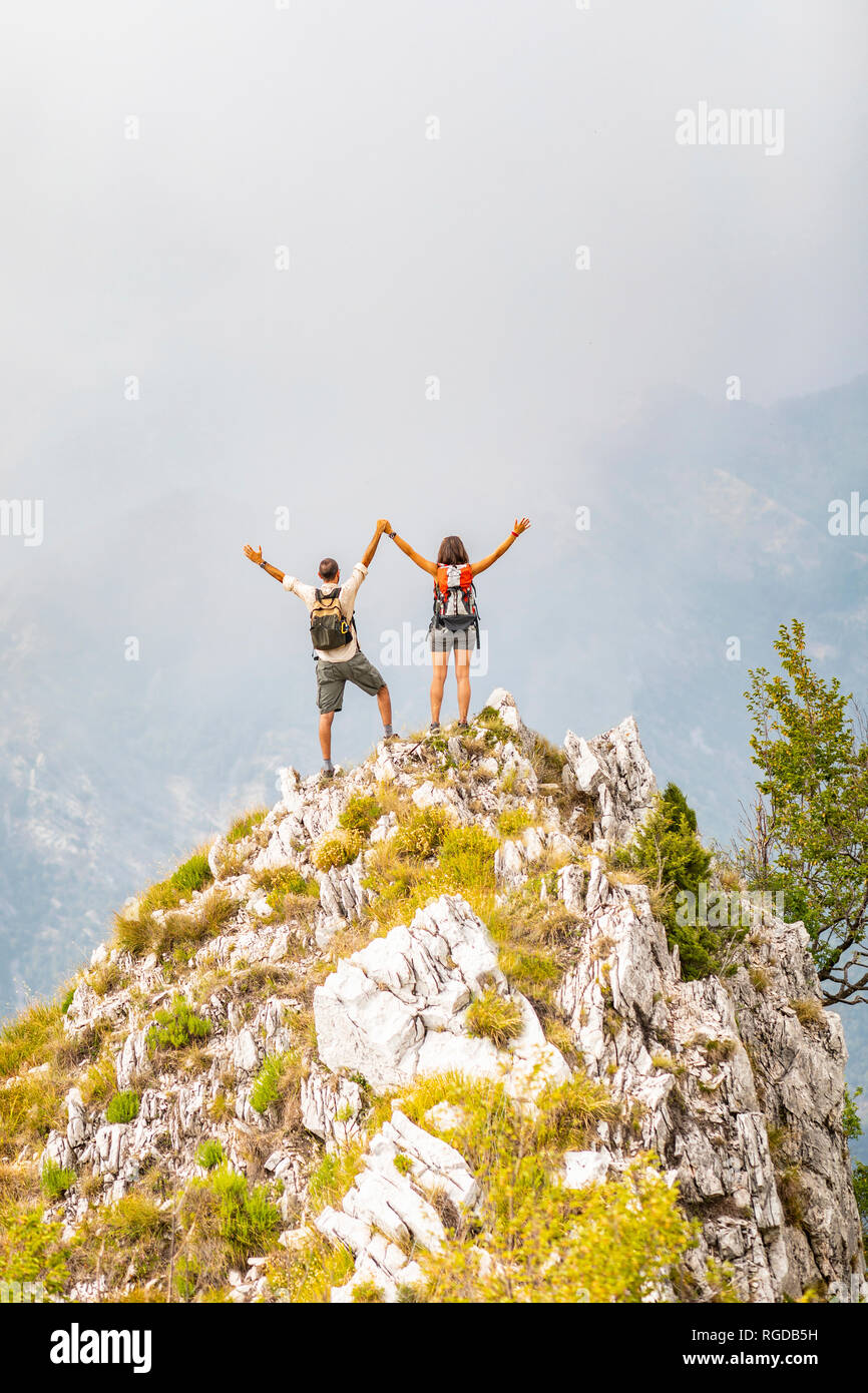 Italy, Massa, happy couple cheering on top of a peak in the Alpi Apuane mountains Stock Photo
