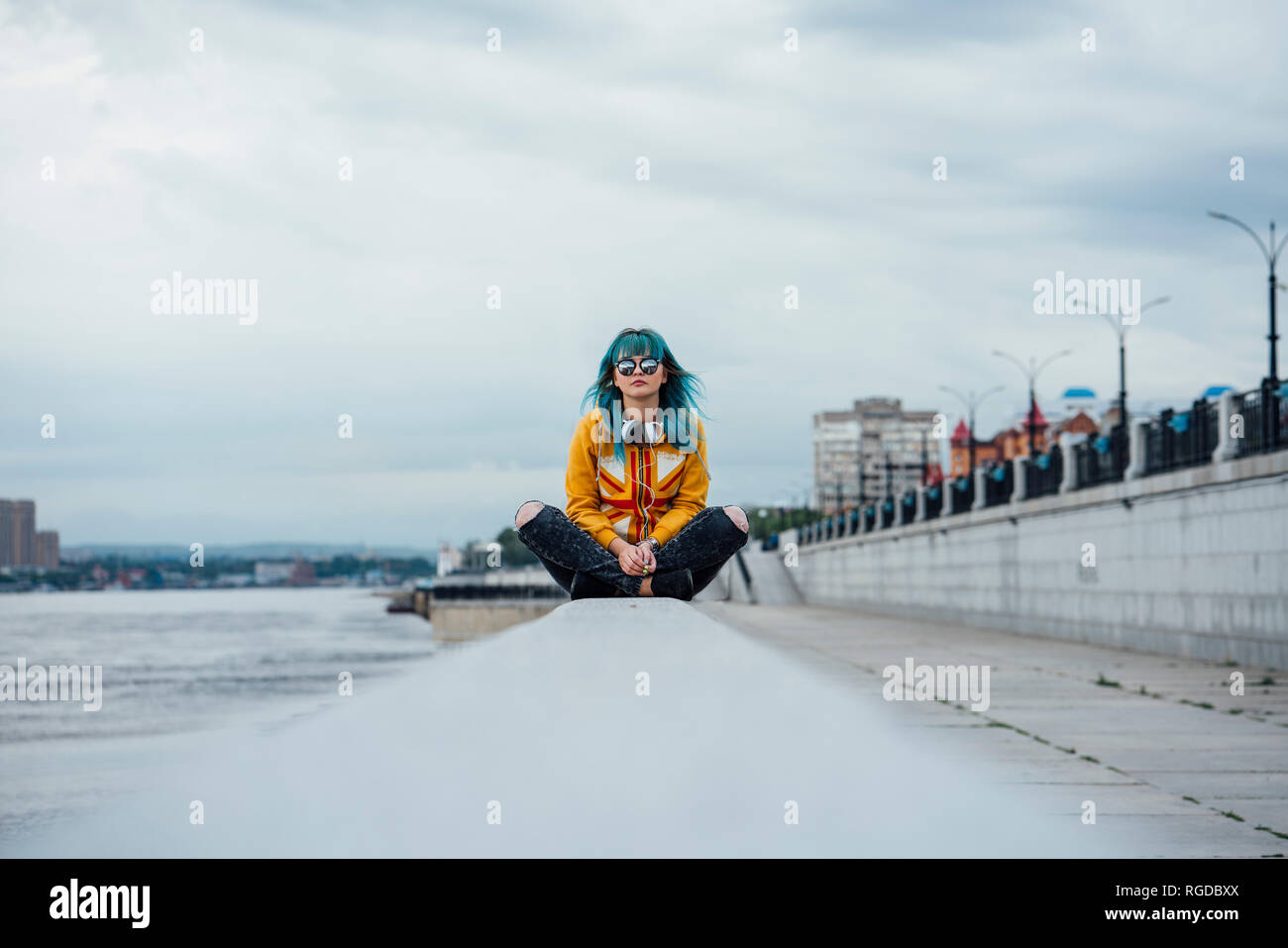 Young woman with dyed blue hair sitting on a wall Stock Photo