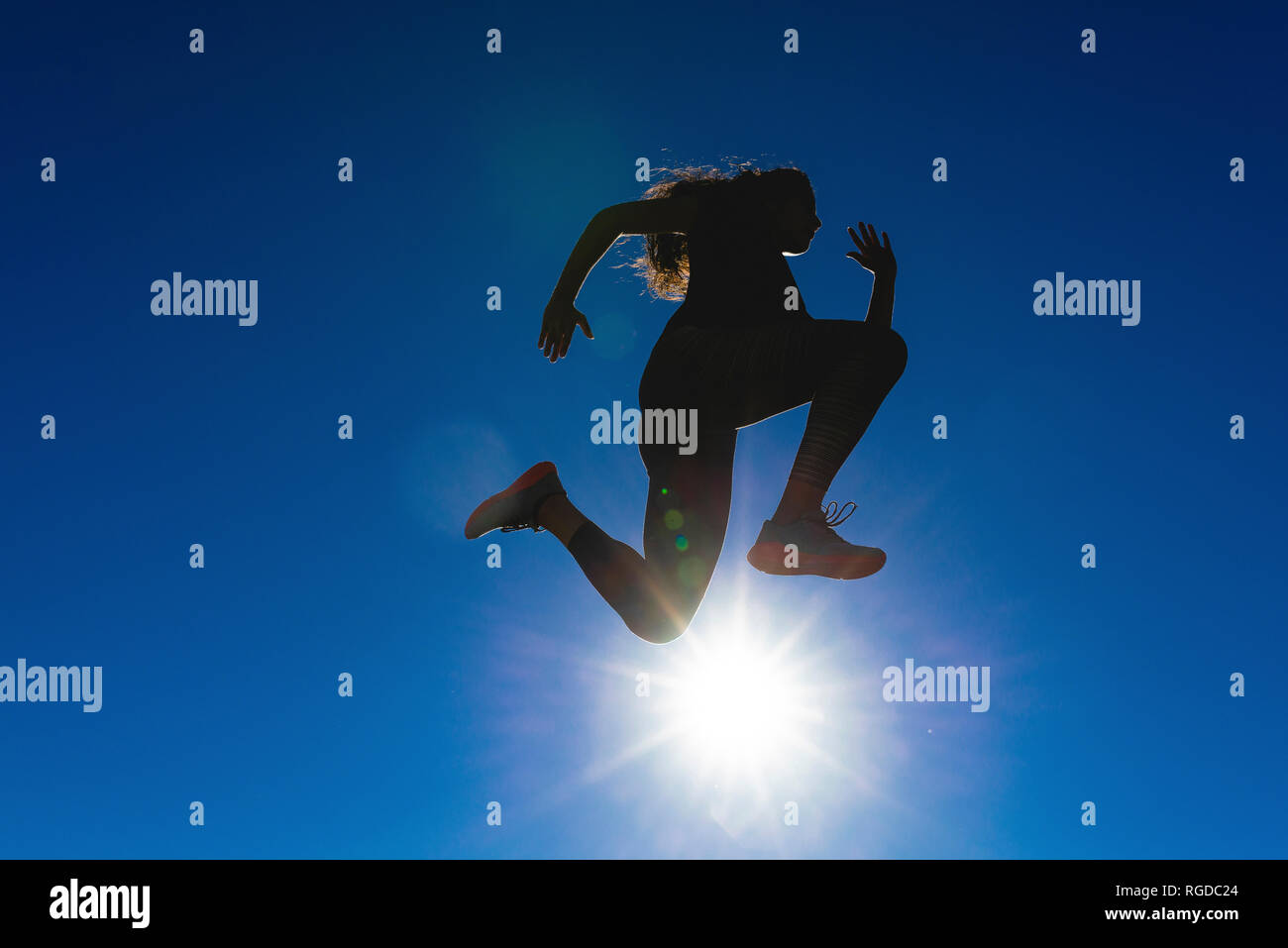 Sportive young woman jumping under blue sky in backlight Stock Photo