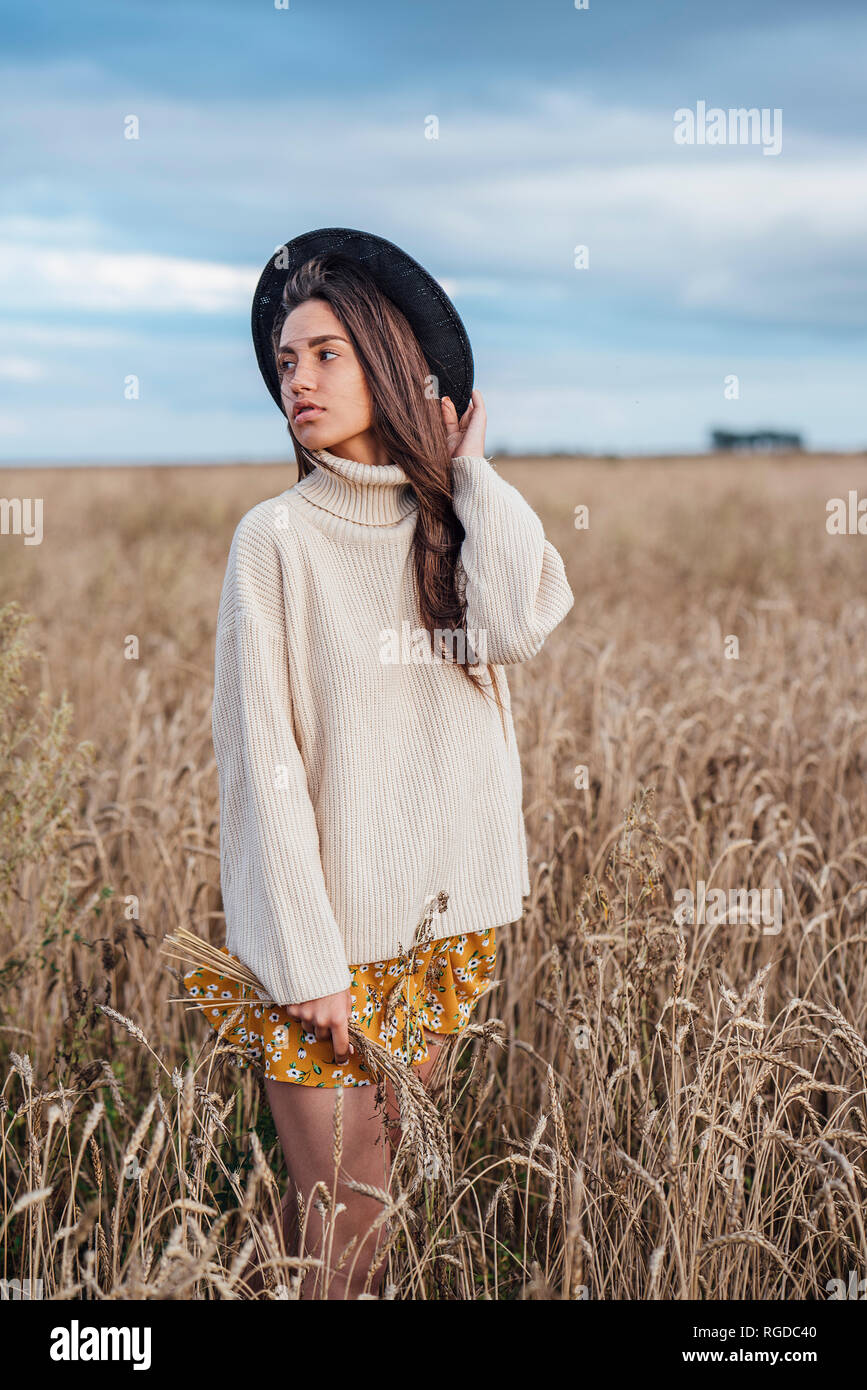 Portrait of young woman wearing hat and oversized turtleneck pullover standing in corn field Stock Photo