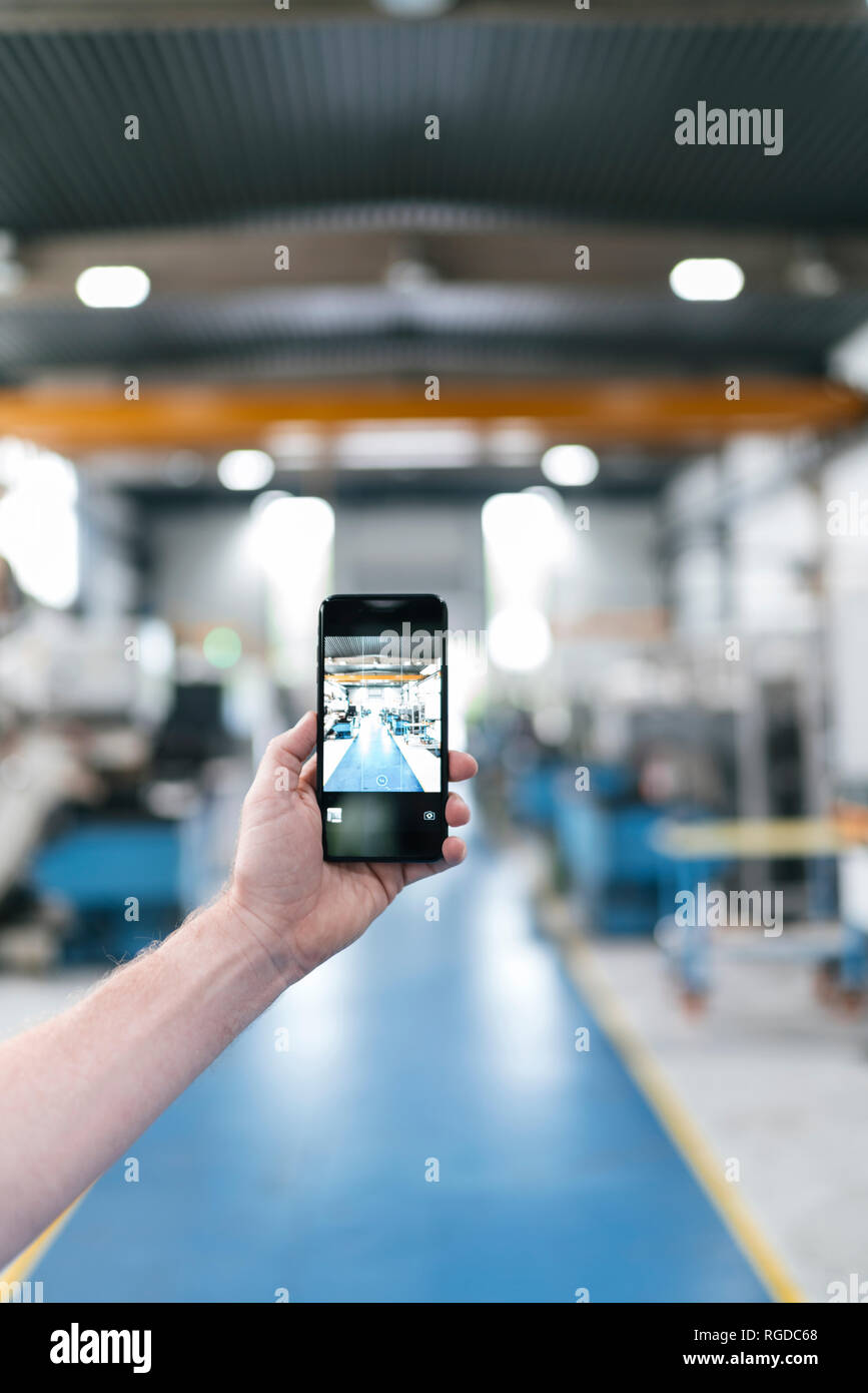 Hand holding smartphone in a factory workshop Stock Photo