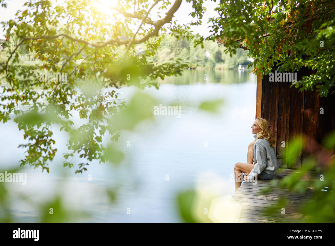 Relaxed woman sitting on wooden jetty at a remote lake Stock Photo