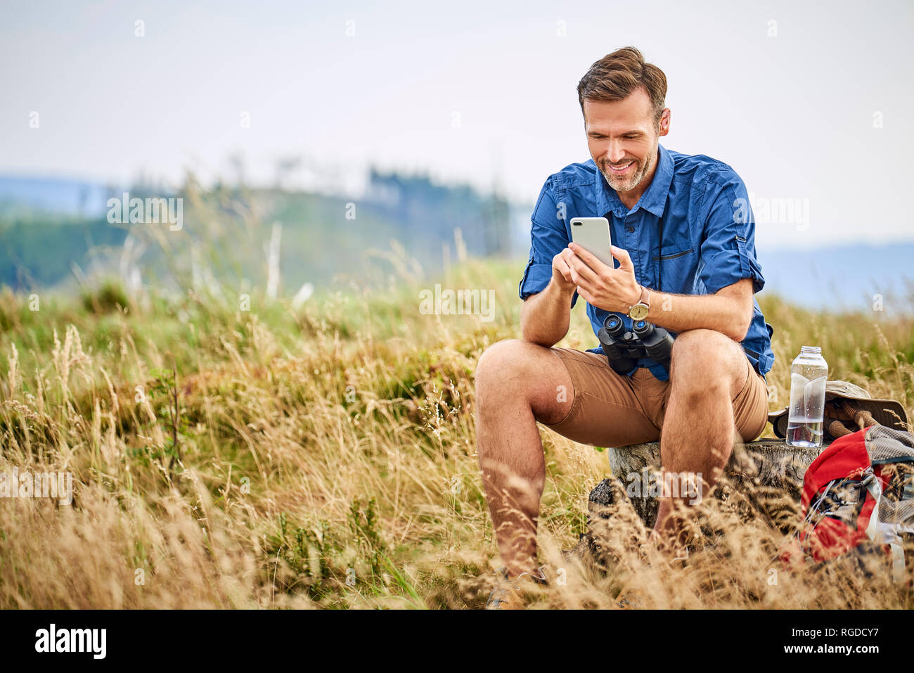Smiling man resting and checking his cell phone during hiking trip Stock Photo