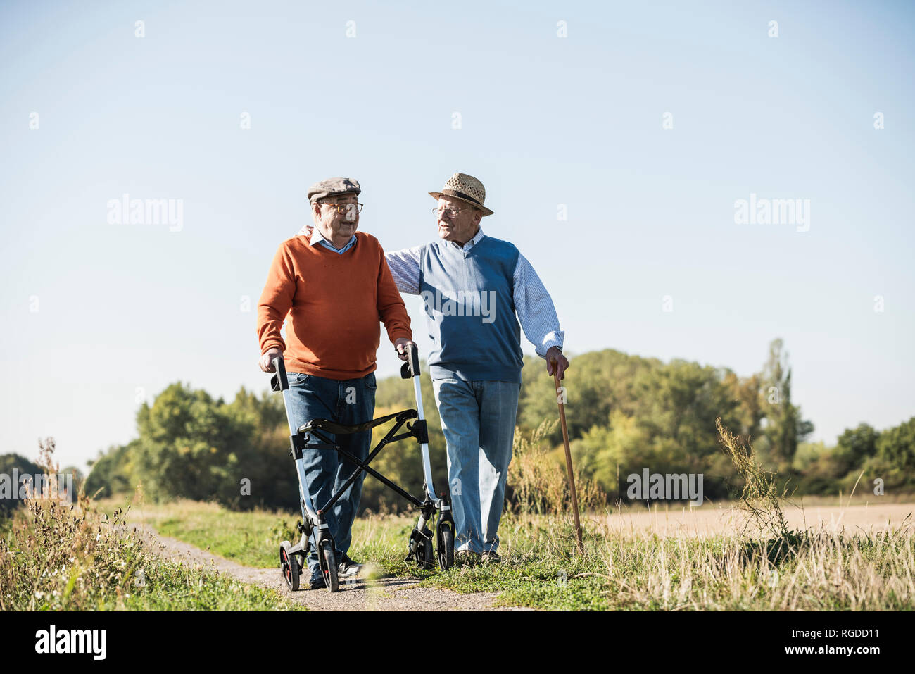 Old friends taking a stroll in the fields with walking stick and wheeled walker, talking about
