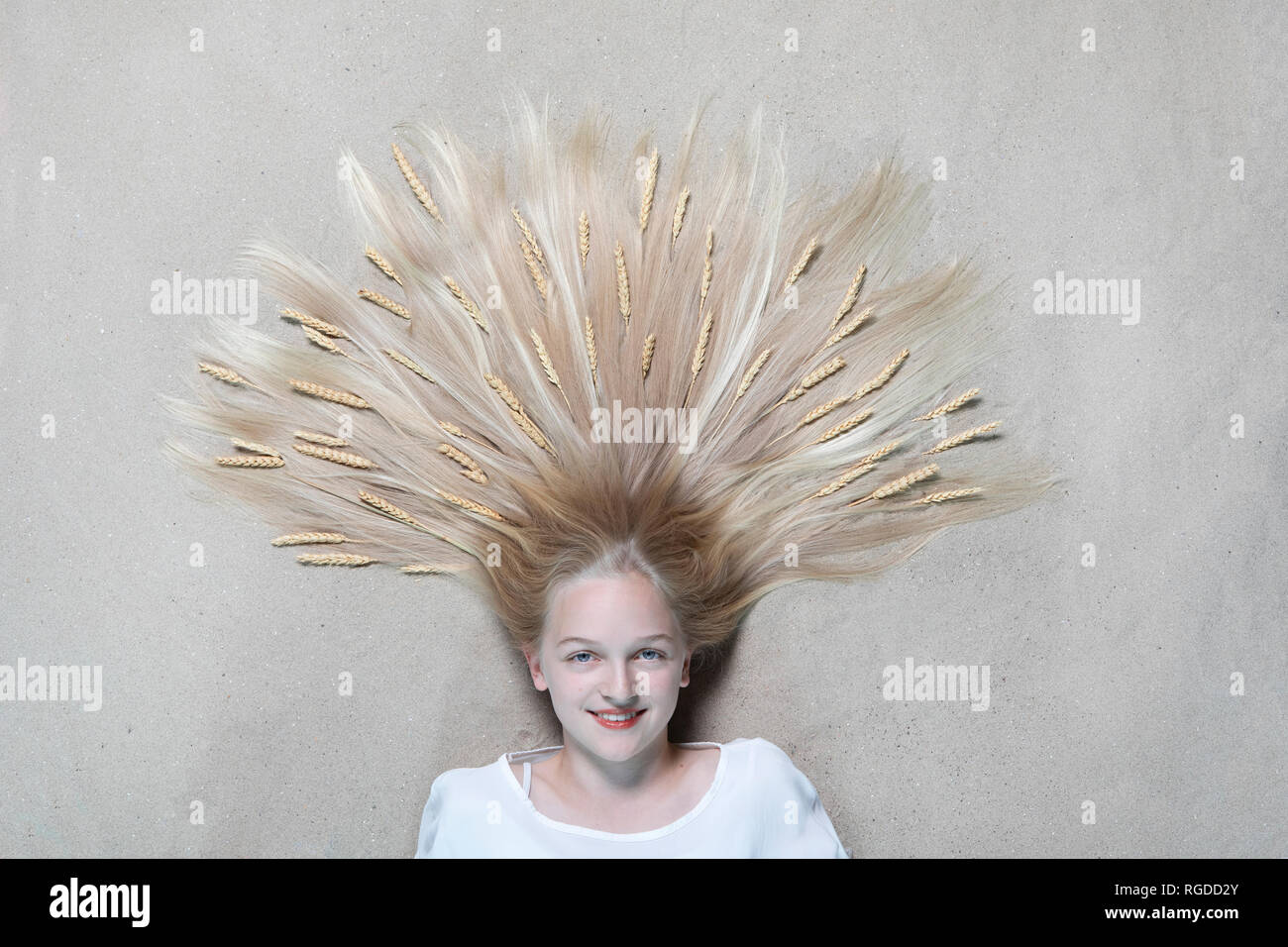 Portrait of smiling girl lying on floor with ears of wheat on hair Stock Photo