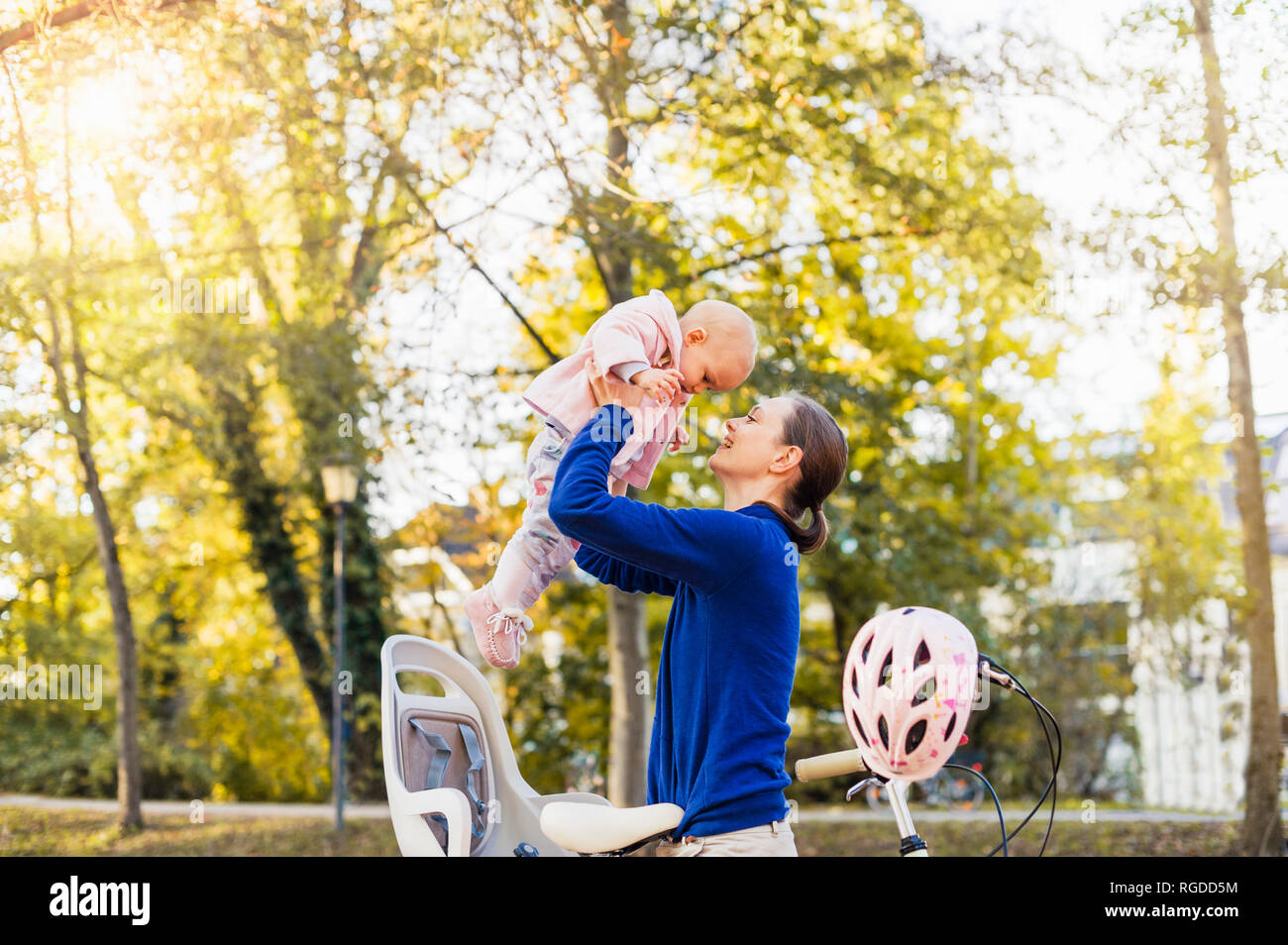 Mother and daughter riding bicycle, lifting baby  from children's seat Stock Photo