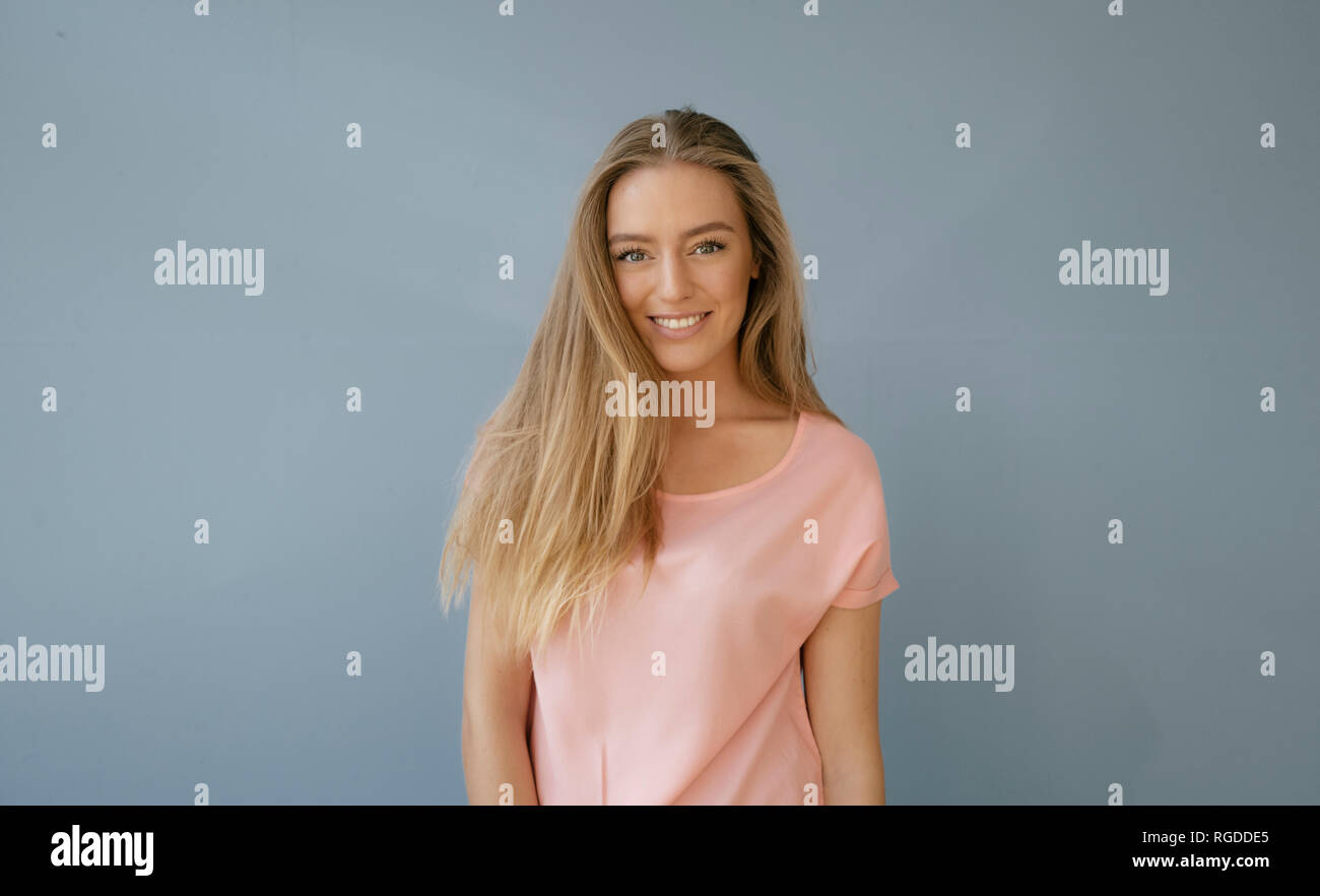 Portrait of smiling young woman wearing pink t-shirt in front of grey background Stock Photo