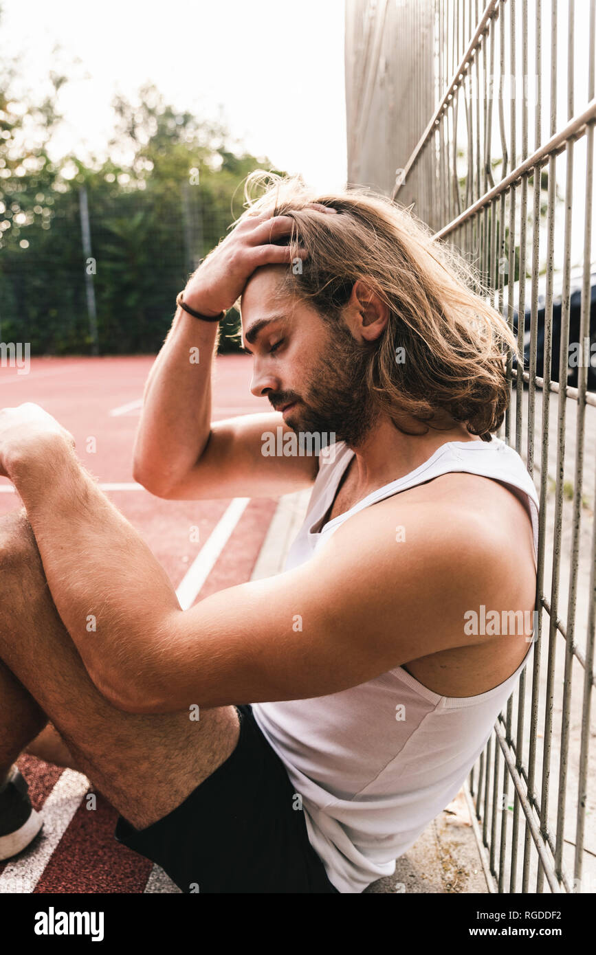 Young man sitting on basketball ground, tired and disappointed Stock Photo