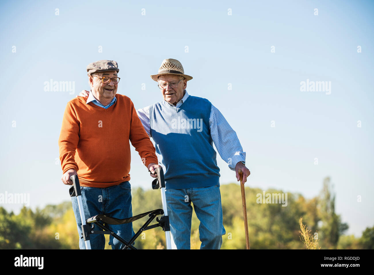 Old friends taking a stroll in the fields with walking stick and wheeled walker, talking about