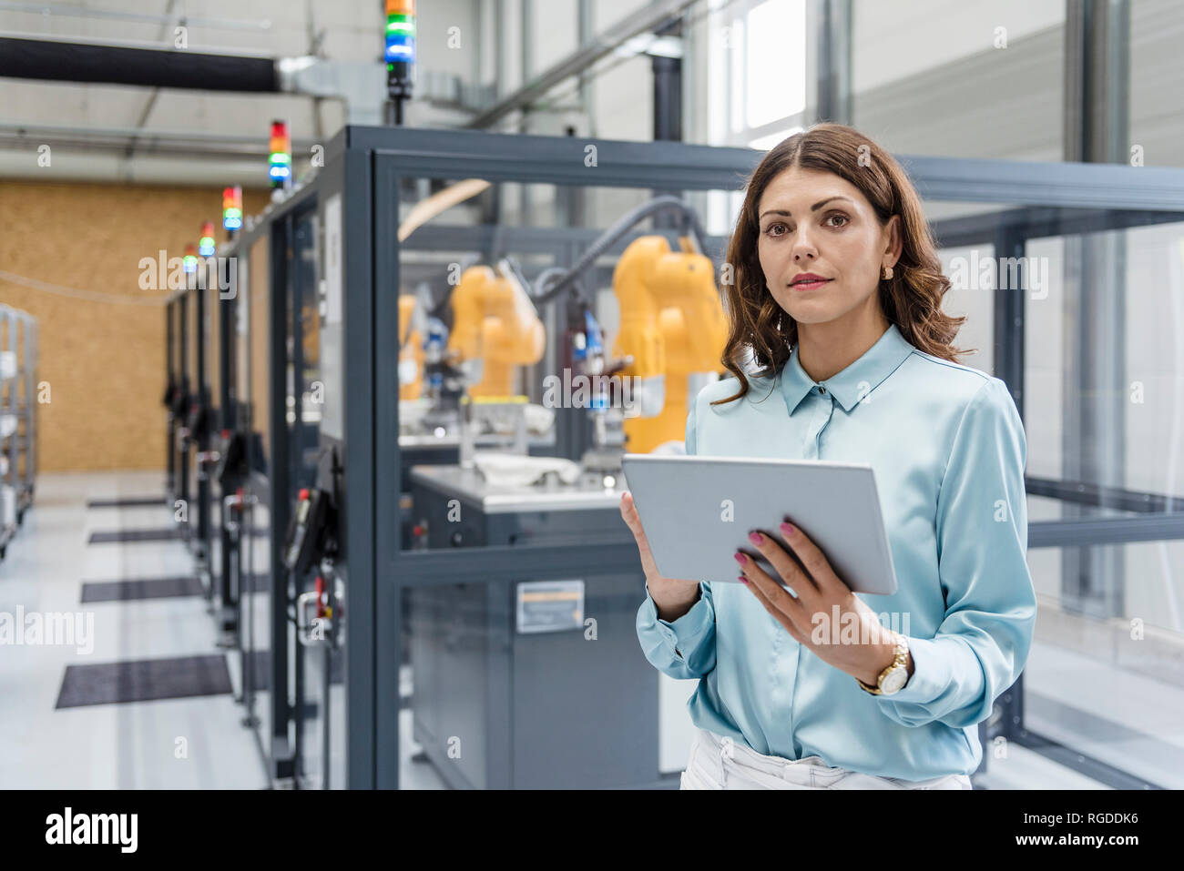 Businesswoman in high tech company controlling industrial robots, using digital tablet Stock Photo