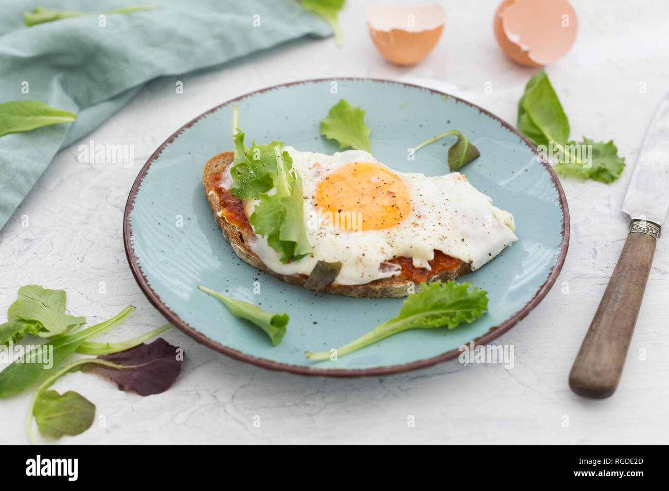Fried egg on slice of brown bread coated with paprika cream on plate Stock Photo