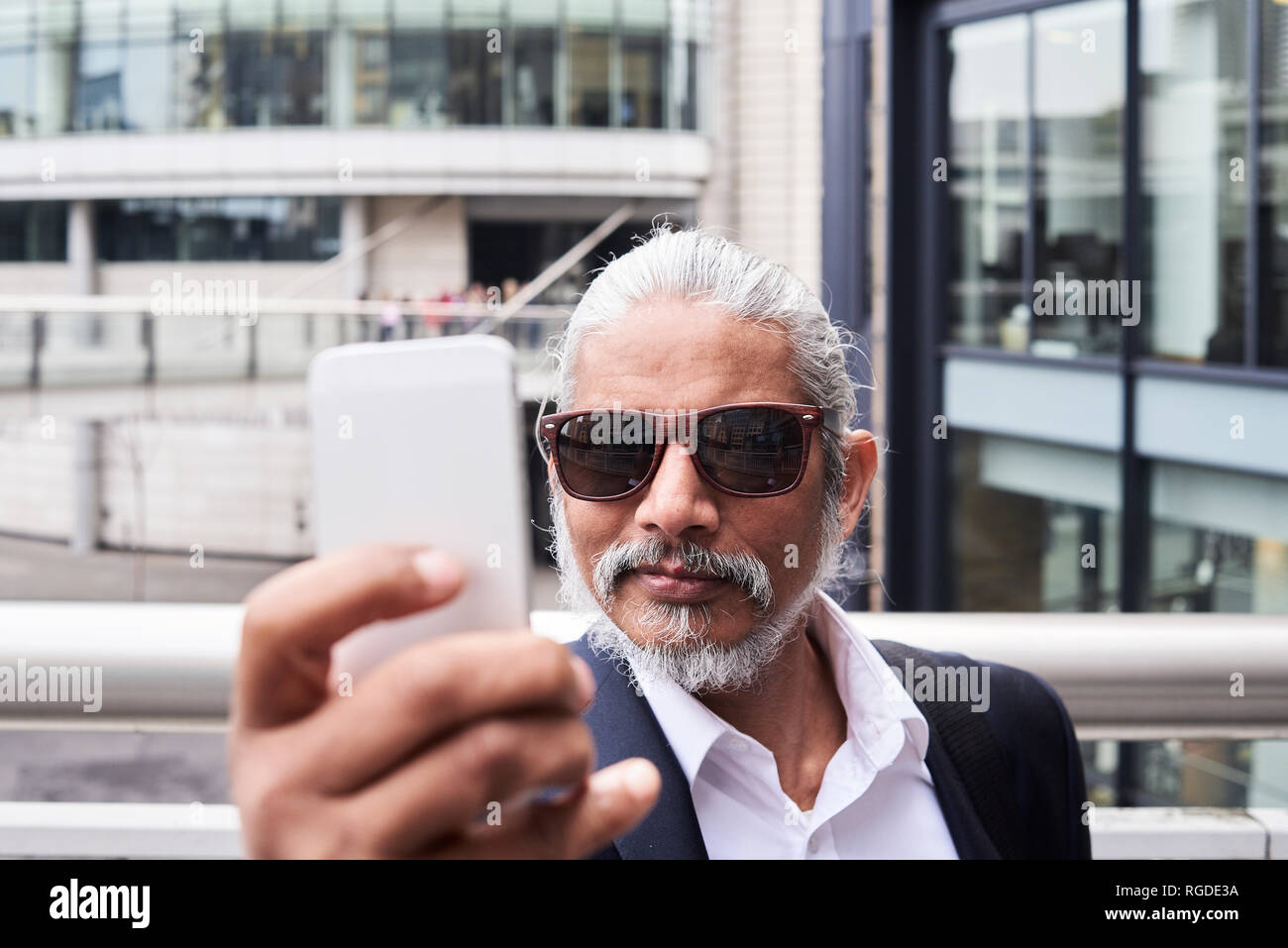 Portrait of grey-haired senior businessman taking selfie with smartphone Stock Photo