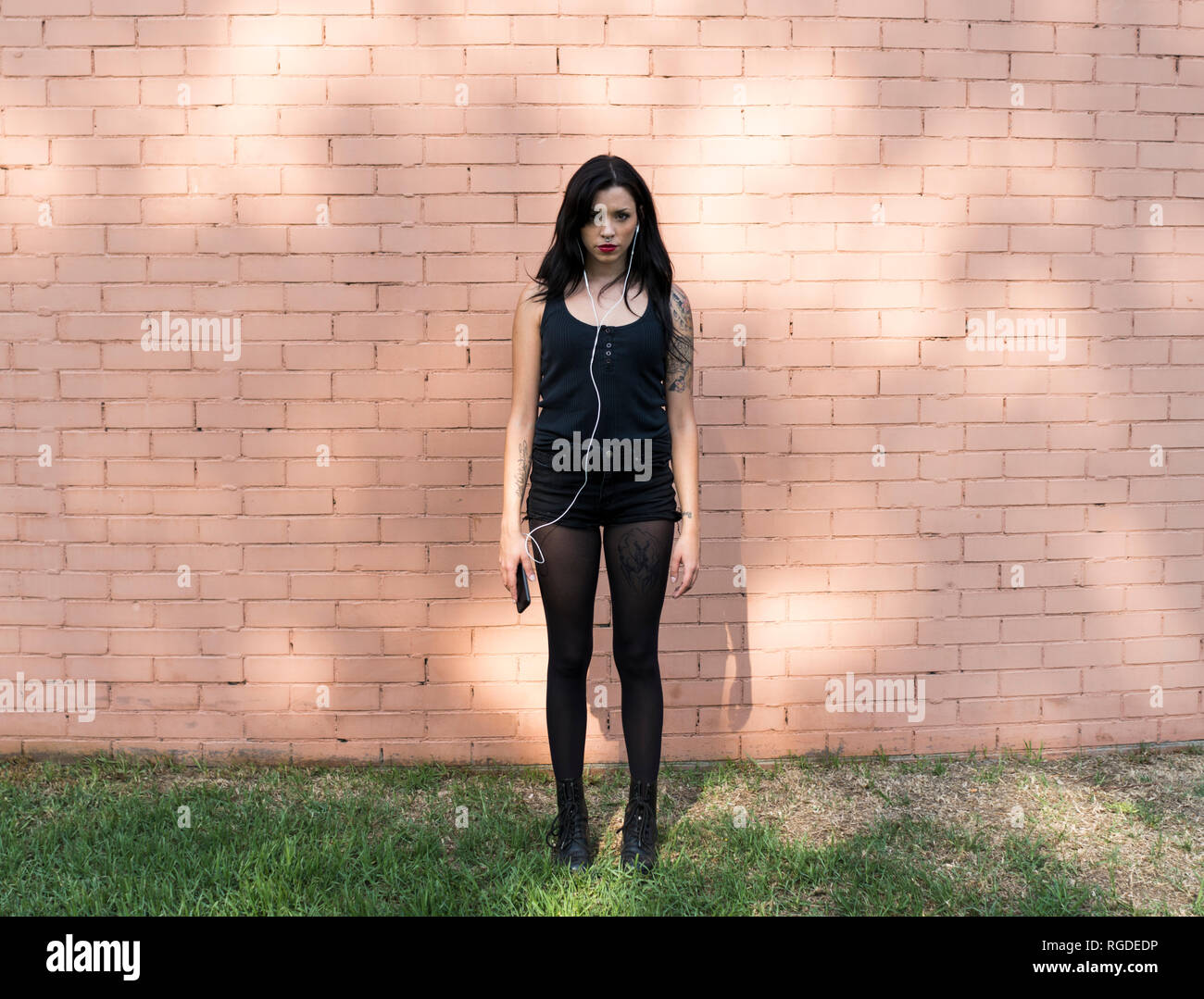 Portrait of young woman with smartphone and earphones dressed in black Stock Photo