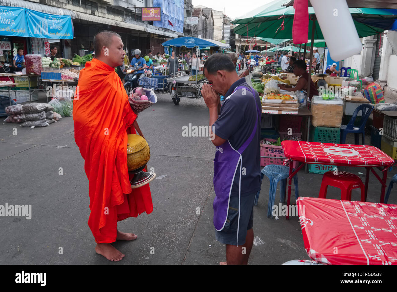 A vendor in the Fresh Market in Phuket Town, Thailand,  honors a Buddhist monk on his alms round with a traditional 'wai', a respectful Thai greeting Stock Photo