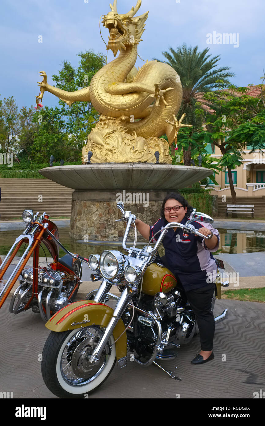 A girl poses on a bike during the annual Phuket Bike Week, behind Hai Leng Ong Statue Golden, depicting a sea dragon; Phuket Town,  Thailand Stock Photo
