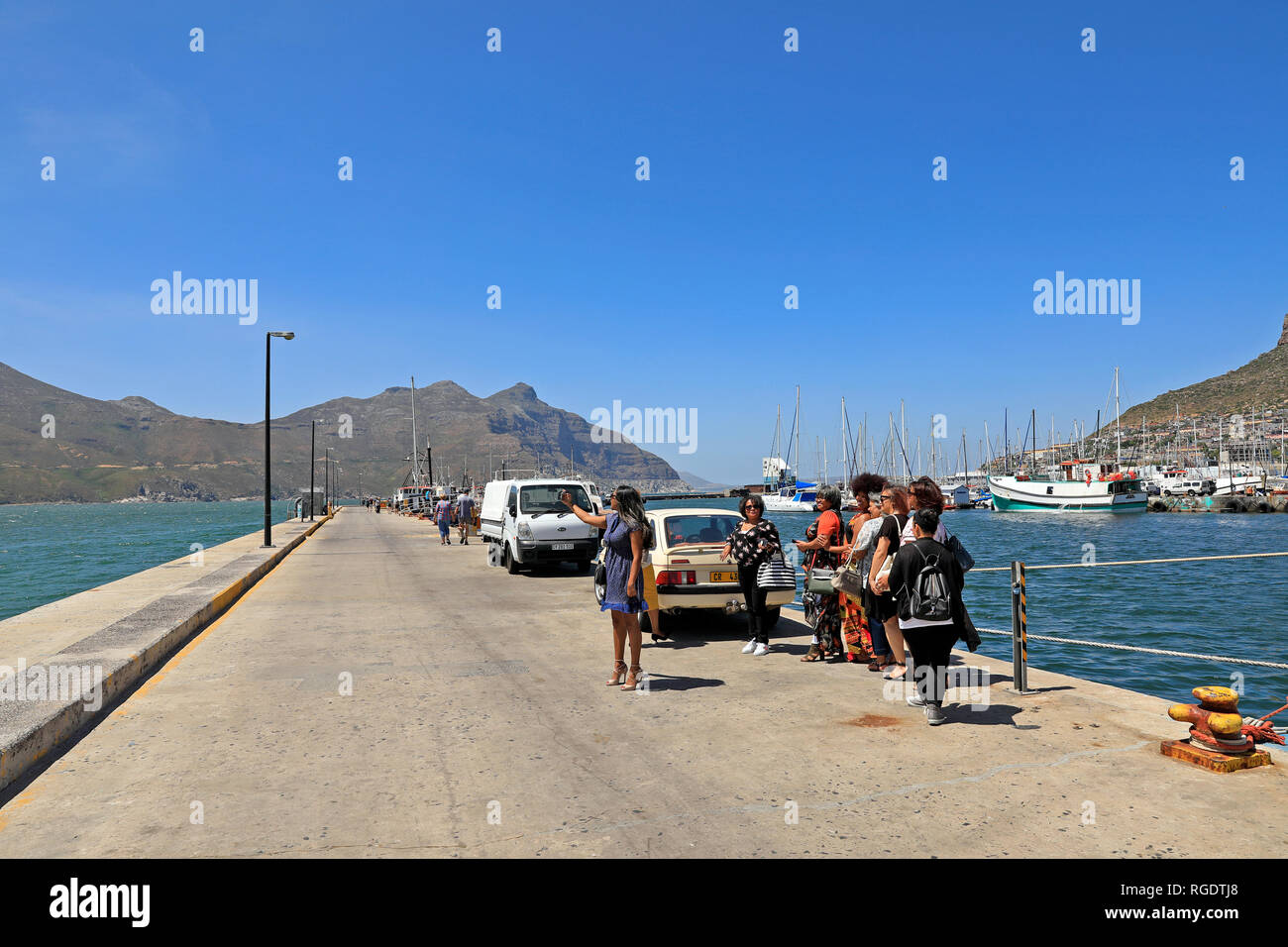 Group of visitors taking selfies along the promenade at Hout Bay harbour near Cape Town, South Africa. Stock Photo
