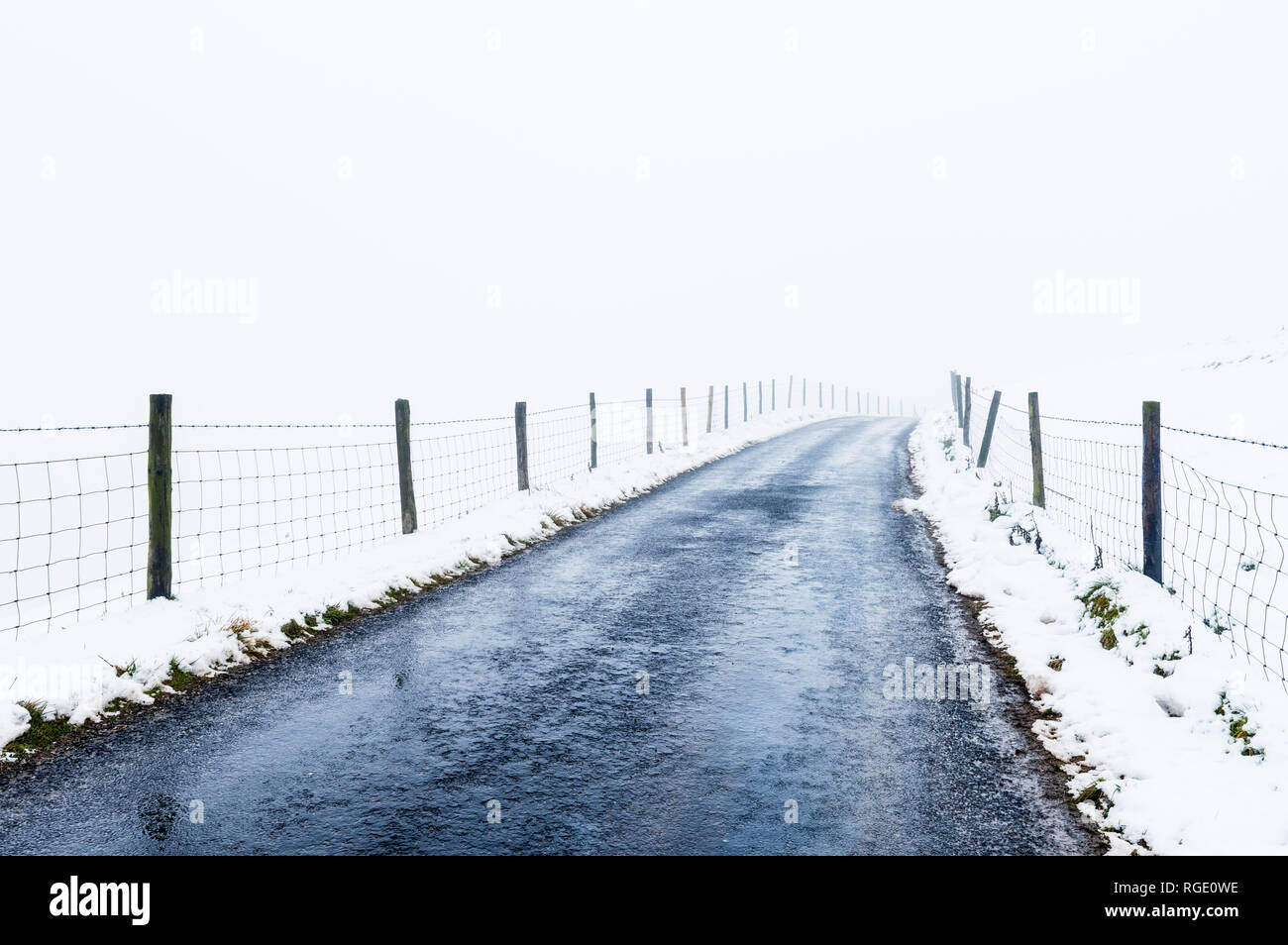 Road surrounded by snow disappearing into the distance Stock Photo